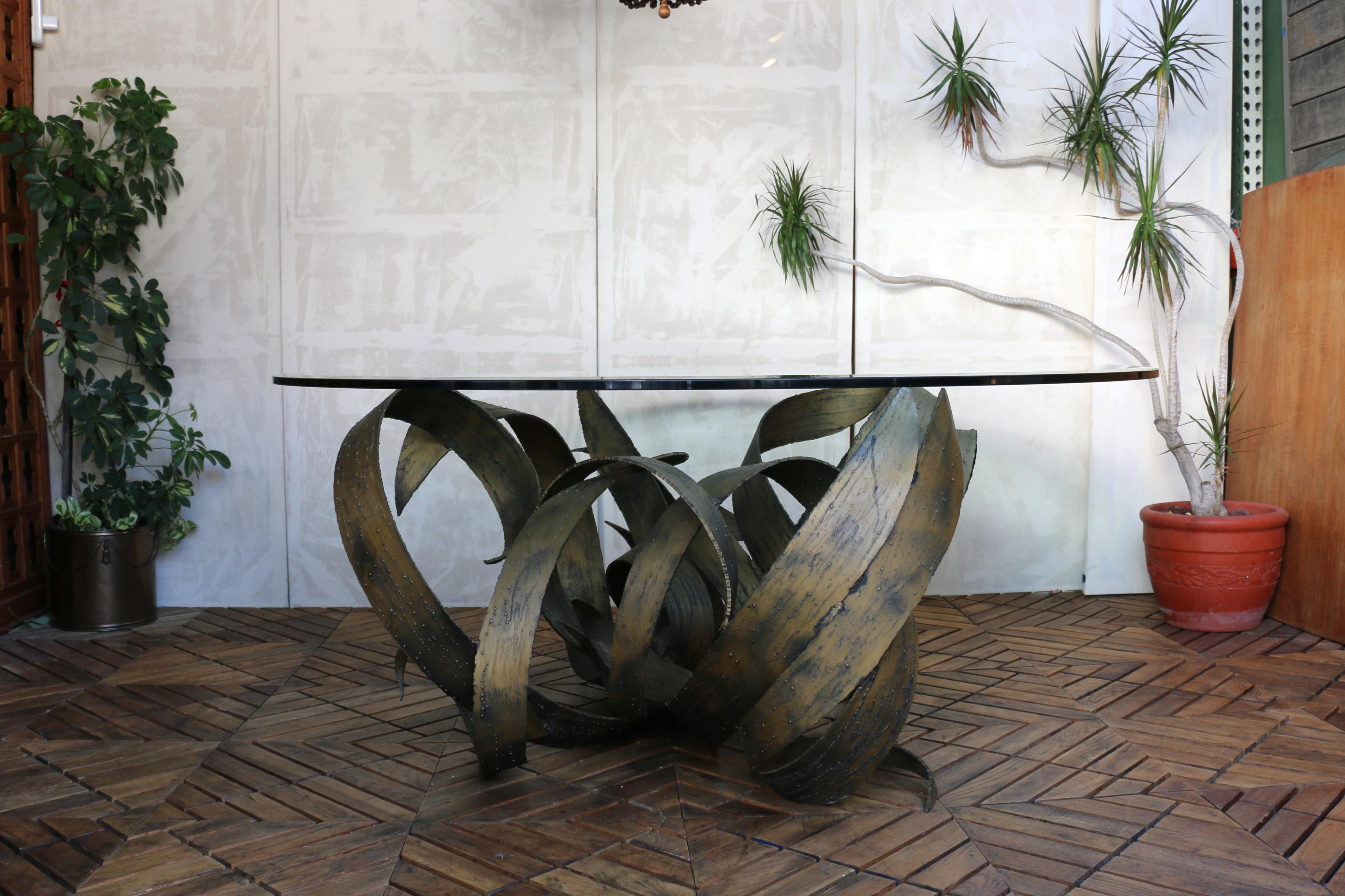 Introducing this striking round glass-top dining table with a unique, sculptural base, original from the 1970s. This stunning piece of furniture is a work of art that cannot be ignored. Its intricate and detailed design is nothing short of