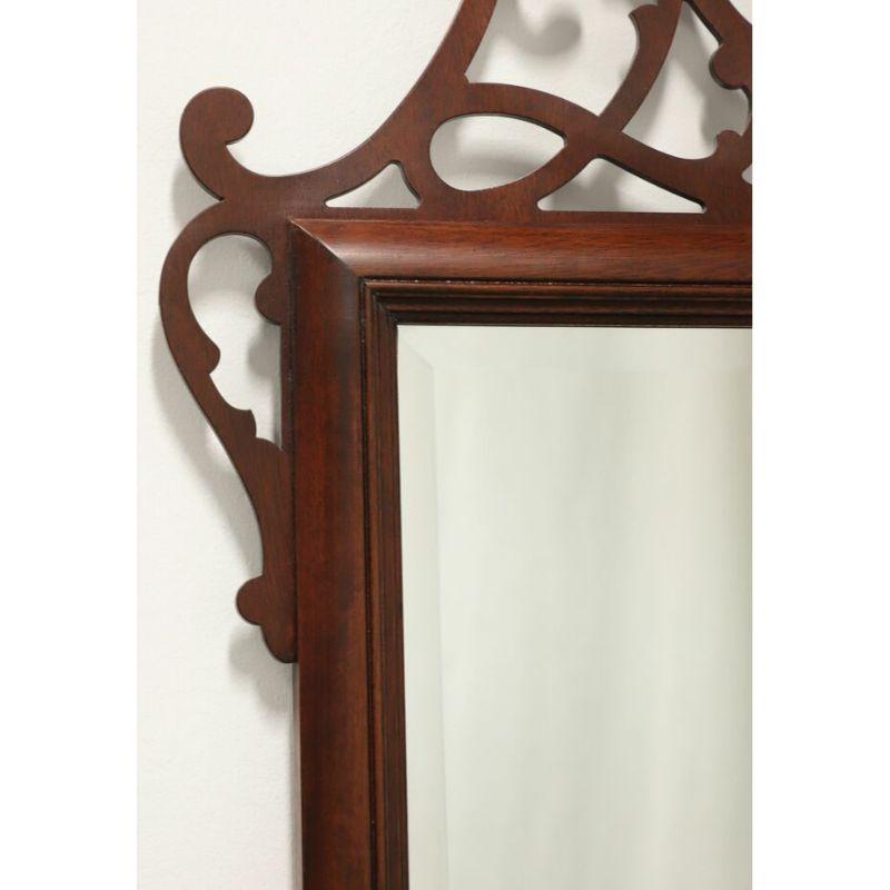 A large Chippendale style wall mirror, unbranded, similar quality to Drexel or Henkel Harris. Bevel edge mirrored glass, mahogany frame with center pediment and finial to top. Decorative carved fretwork to top and bottom. Made in the USA in the late