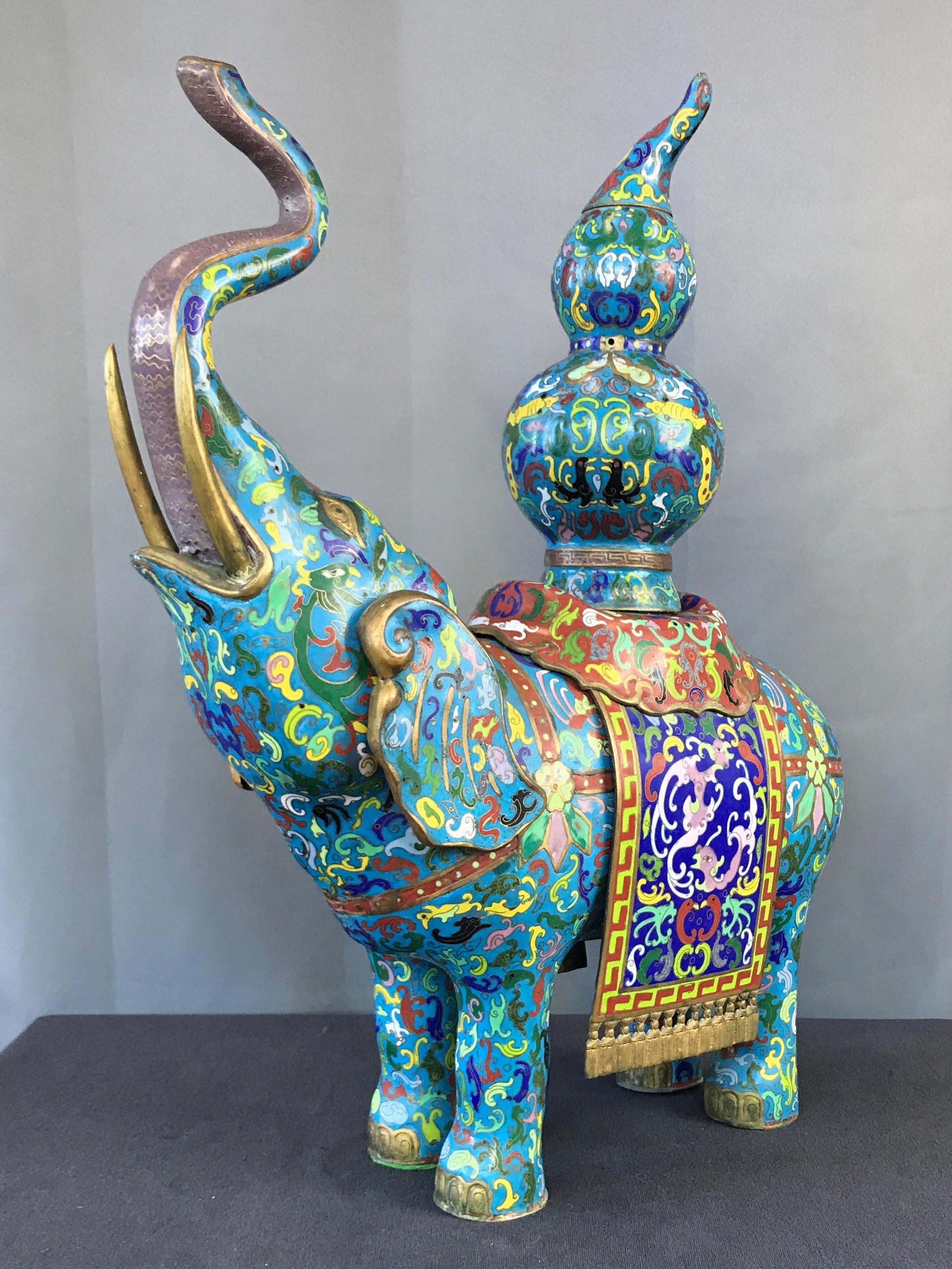 A large and colorful Chinese brass & copper cloisonné elephant vessel, circa mid-20th century.

Elephant with proudly raised trunk carries on its back a removable traditional gourd-shaped form with lid, all of which are hollow and pierced by