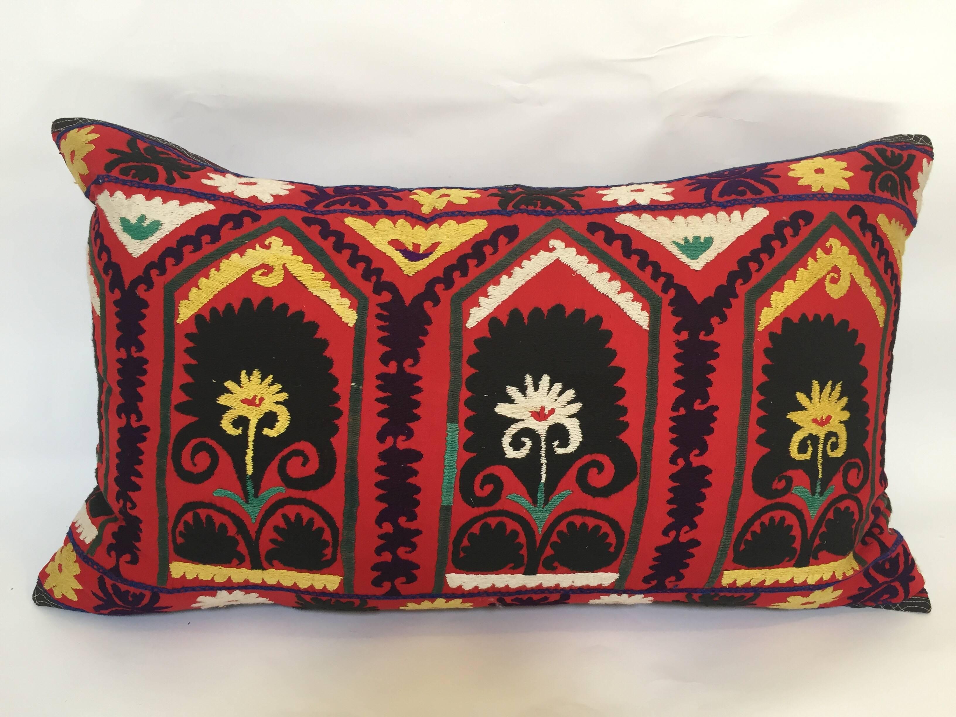 Large vintage colorful Suzani embroidery lumbar pillow red embroidered with colorful threads.
A reddish embroidered pillow with flower motifs and arches In shades of black, red, yellow, white, magenta, kelly green, with linen backing and zipper in