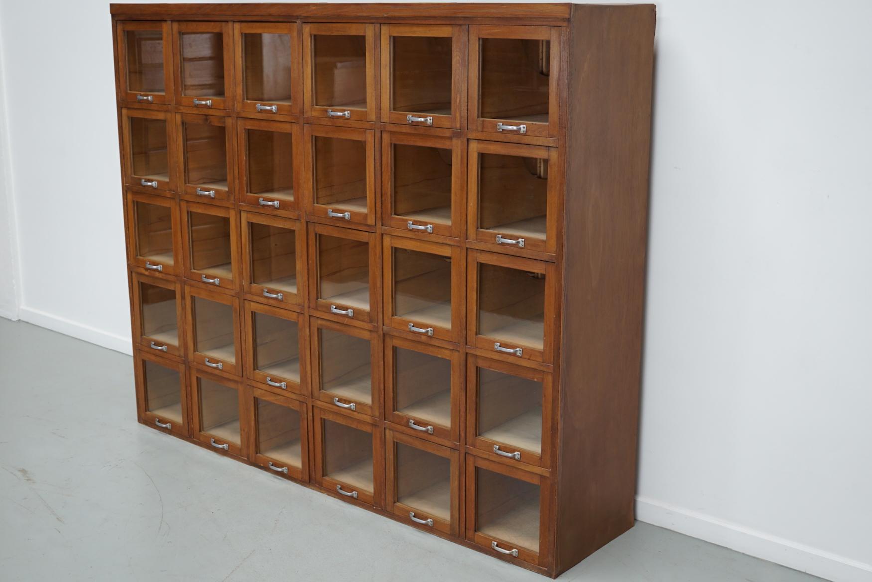 Este mueble de mercería se fabricó durante la década de 1950 en Alemania. Tiene 30 cajones grandes de haya con frentes de cristal y tiradores metálicos. Originalmente se utilizaba en una tienda de ropa de cama. Las dimensiones interiores de los
