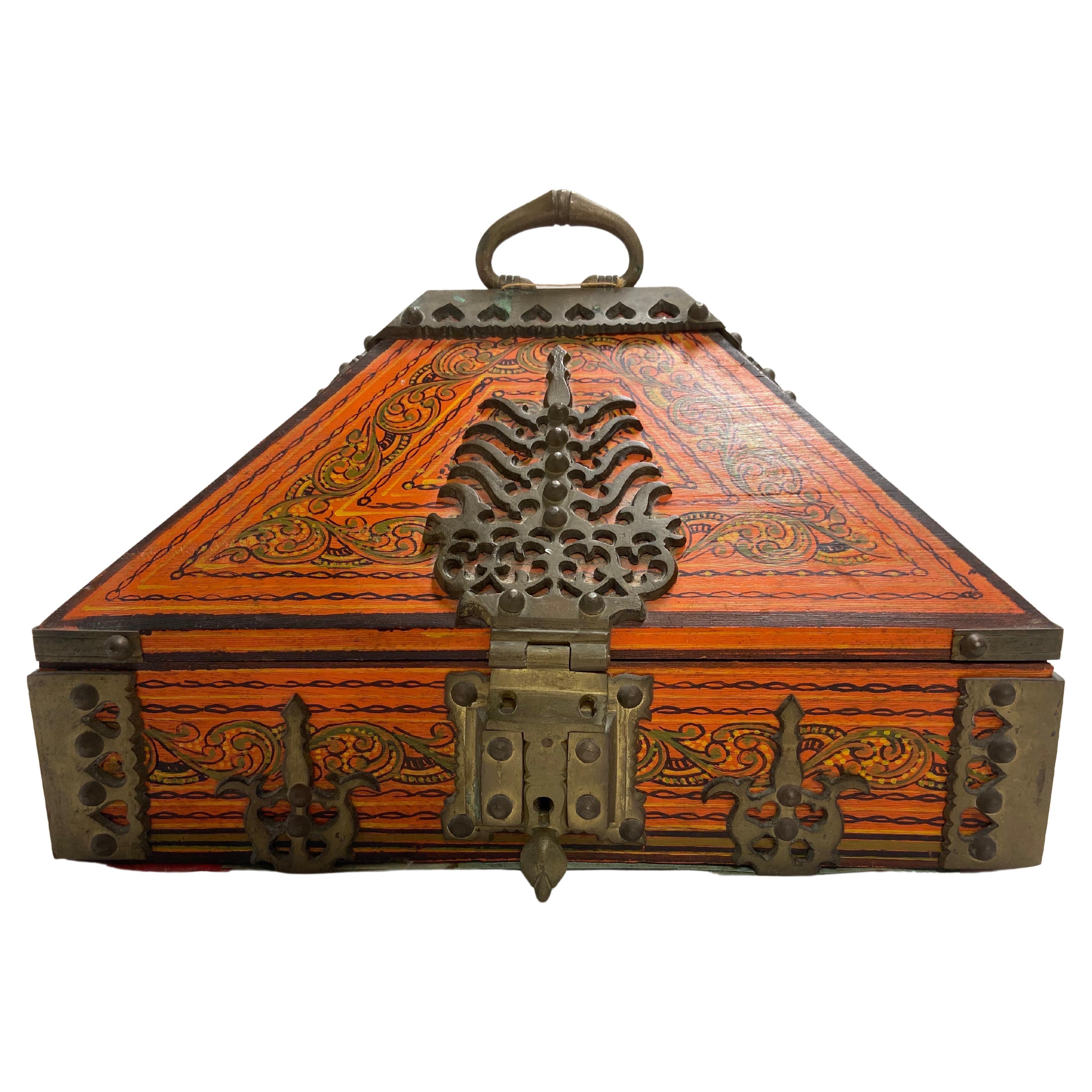 A vintage Indian Dowry box in orange paint with beautiful hand painted details and decorations, secured with ornate and scrolling brass hinges, handle and clasp. The box also has an interior compartment with hand painted decoration as well. A bit