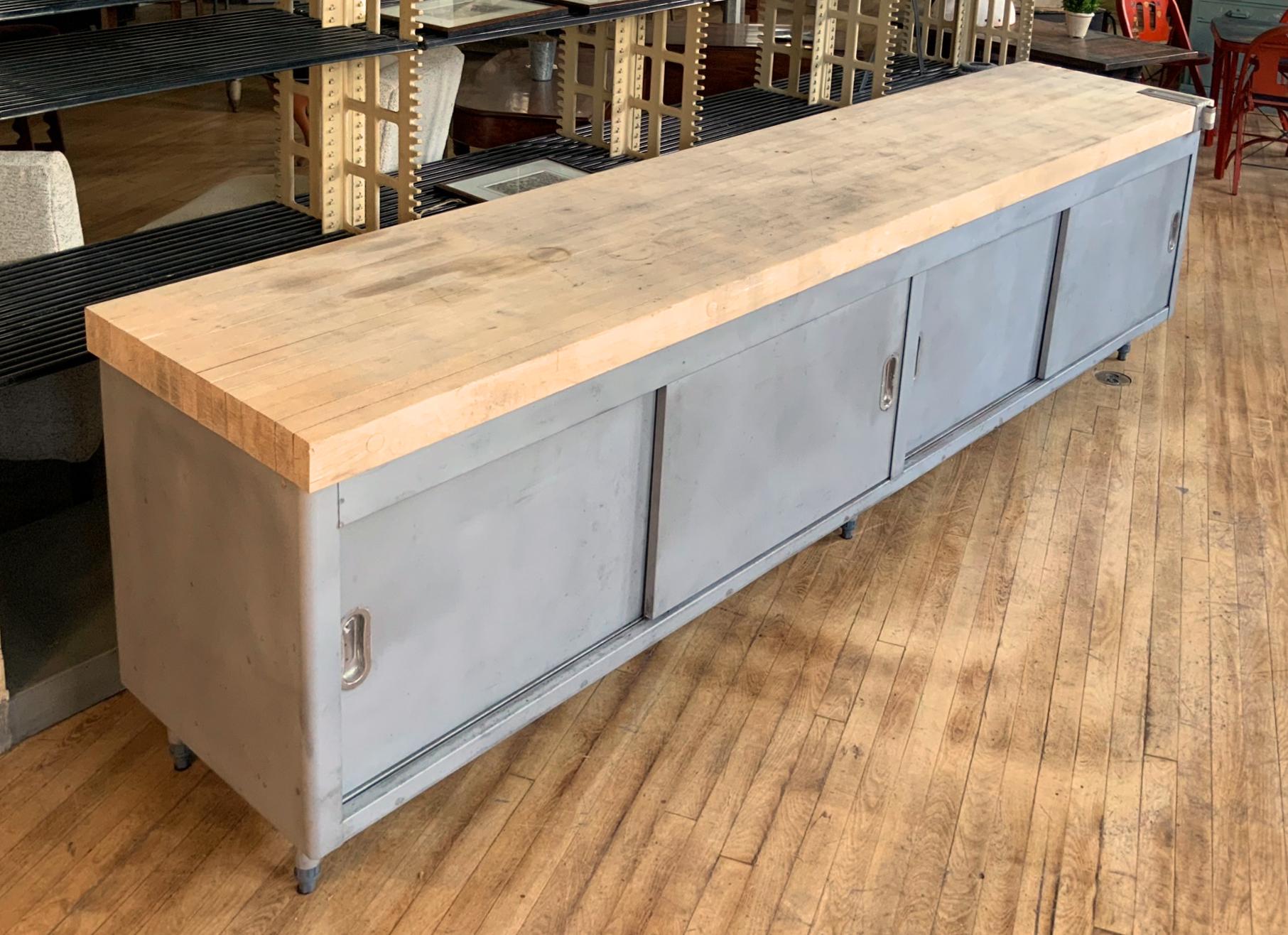 A very nice and well made galvanized steel cabinet with a very thick butcherblock top. The cabinet having full storage behind two pairs of sliding doors, each side with a full width shelf. And the whole raised on steel legs.