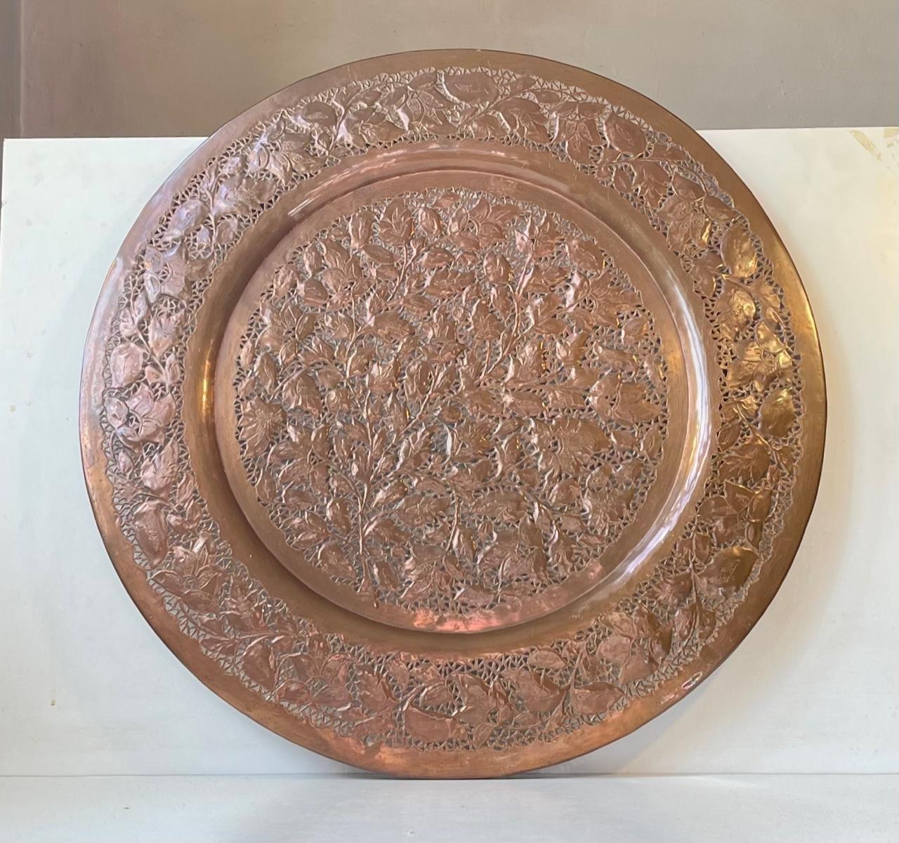 Extra-large (57 cm) plateau persan en cuivre décoré de feuilles et de fleurs avec des perforations complexes. Il a été fabriqué au Pakistan ou en Inde dans les années 1960 ou avant. Il peut être utilisé comme plateau pour servir et peut être