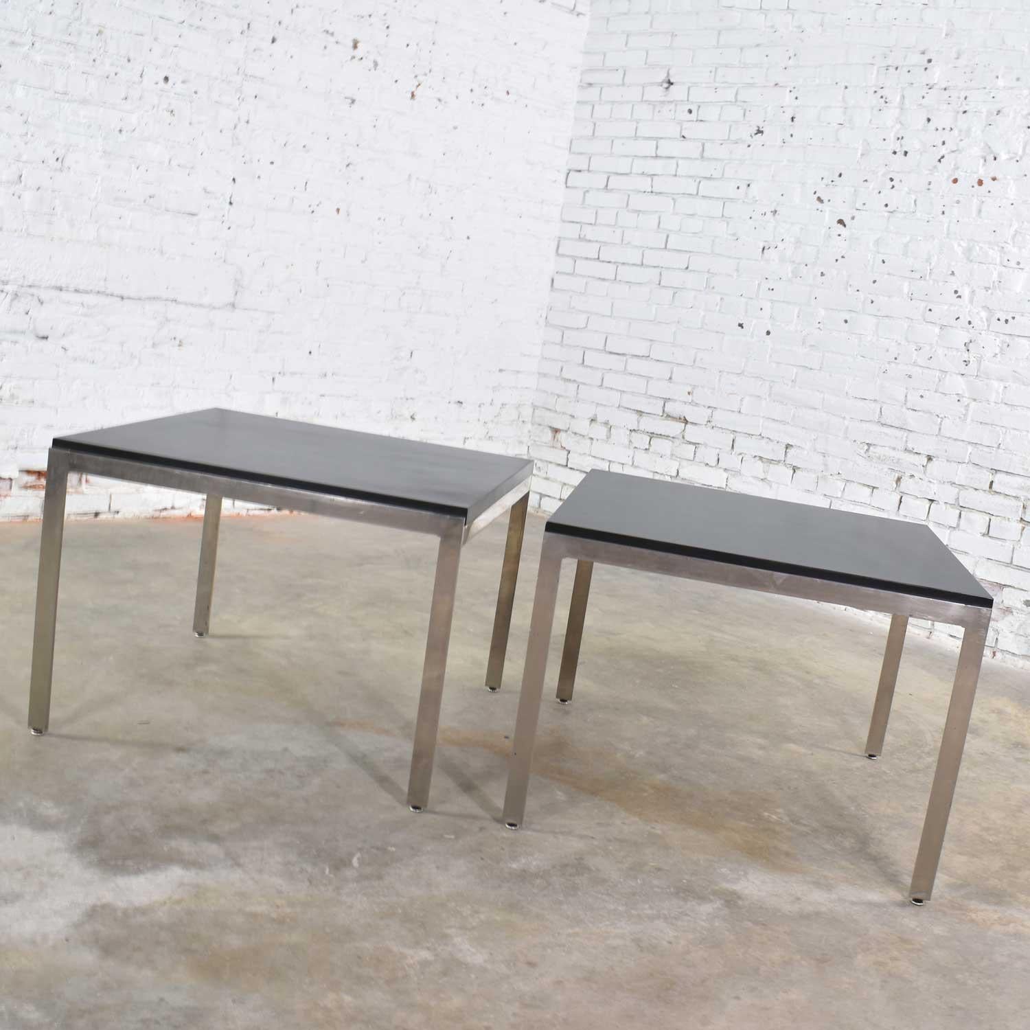 Very handsome pair of stainless steel based large square end tables with black laminate tops. They are in wonderful vintage condition. The stainless may have some small signs of age and use but nothing major. The laminate tops have received a fresh