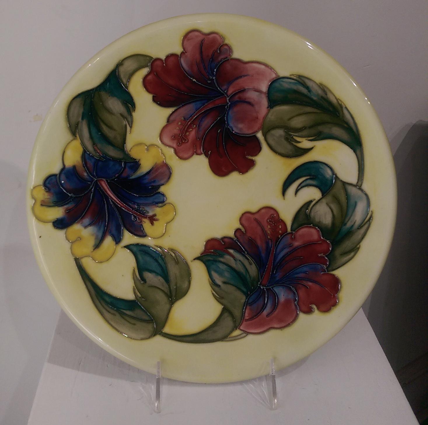Large beautiful charger plate is decorated in the much sought after luscious hibiscus flowers in coral, pink, blue and yellow on a field of soft yellow. Measures approximate size: 12 inches in diameter. The bottom is signed and marked in blue,