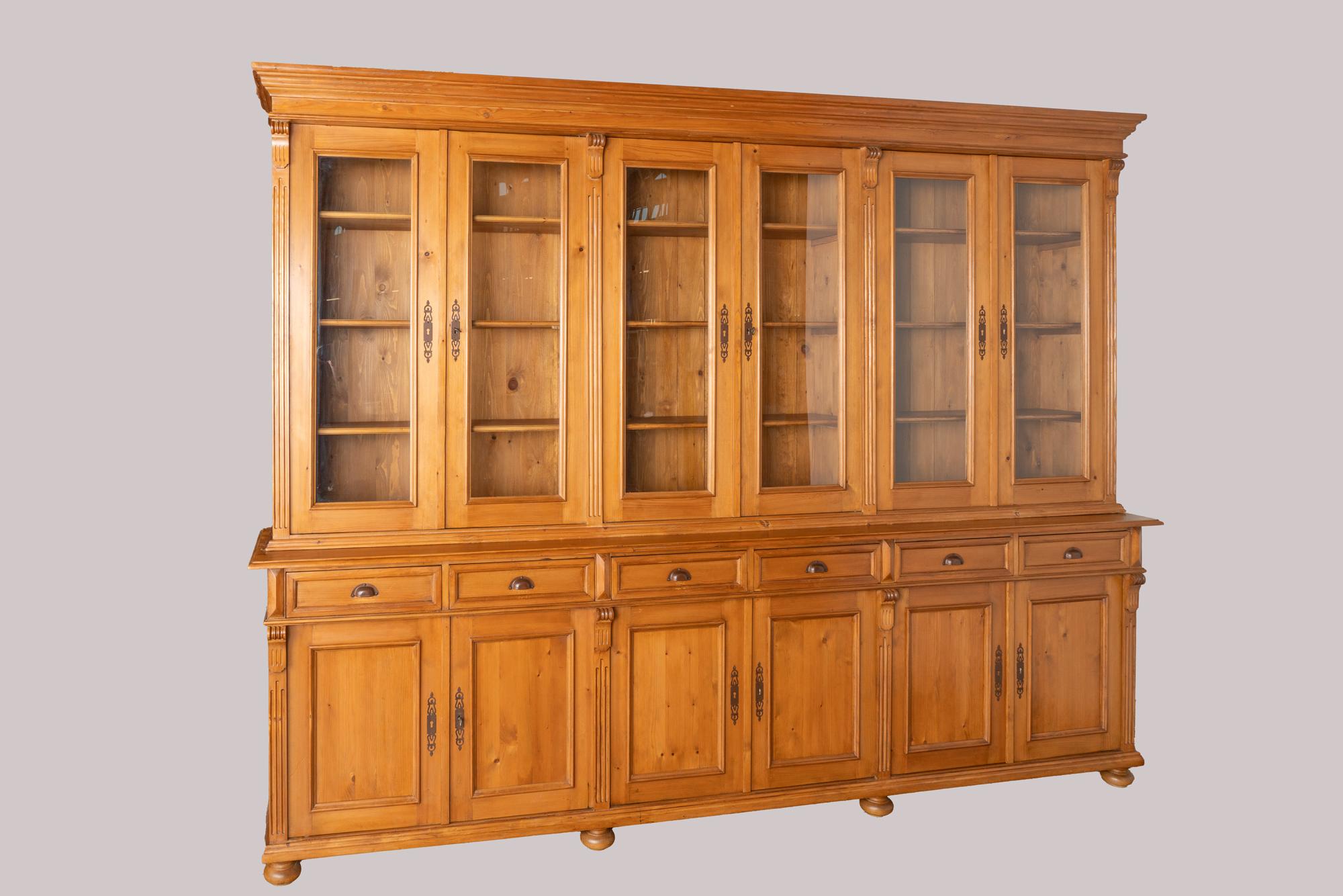 This striking large pine bookcase or display wall unit is a reproduction made in Europe and breaks down into two large cabinets.
The pine has a warm, inviting patina and country appeal thanks to a satin wax finish.
The upper display section with six