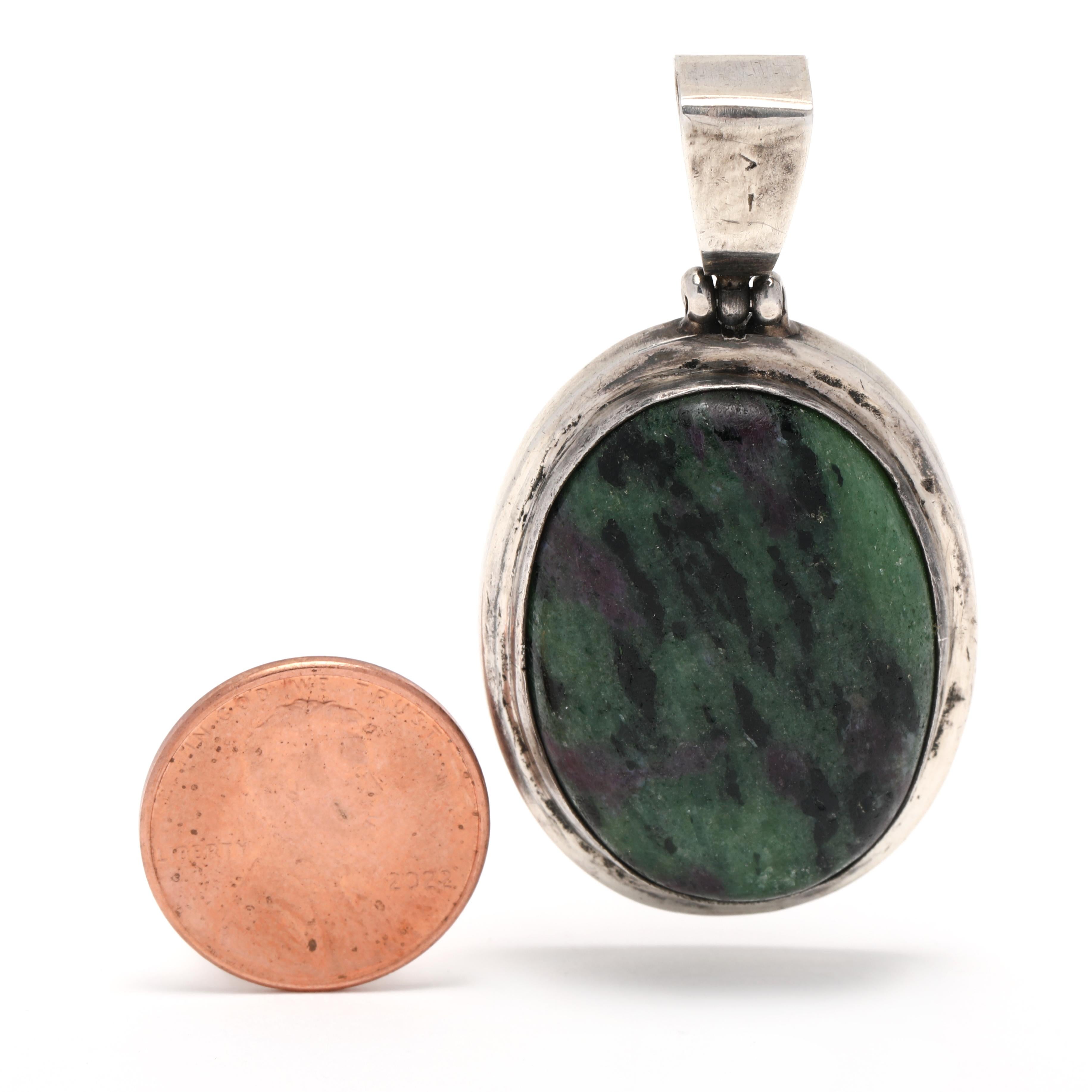 This stunning vintage pendant features a large oval ruby in zoisite stone, set into a sterling silver bezel. The unique gemstone is naturally deep green with contrasting red ruby crystals throughout. It measures 2 inches in length and hangs from a