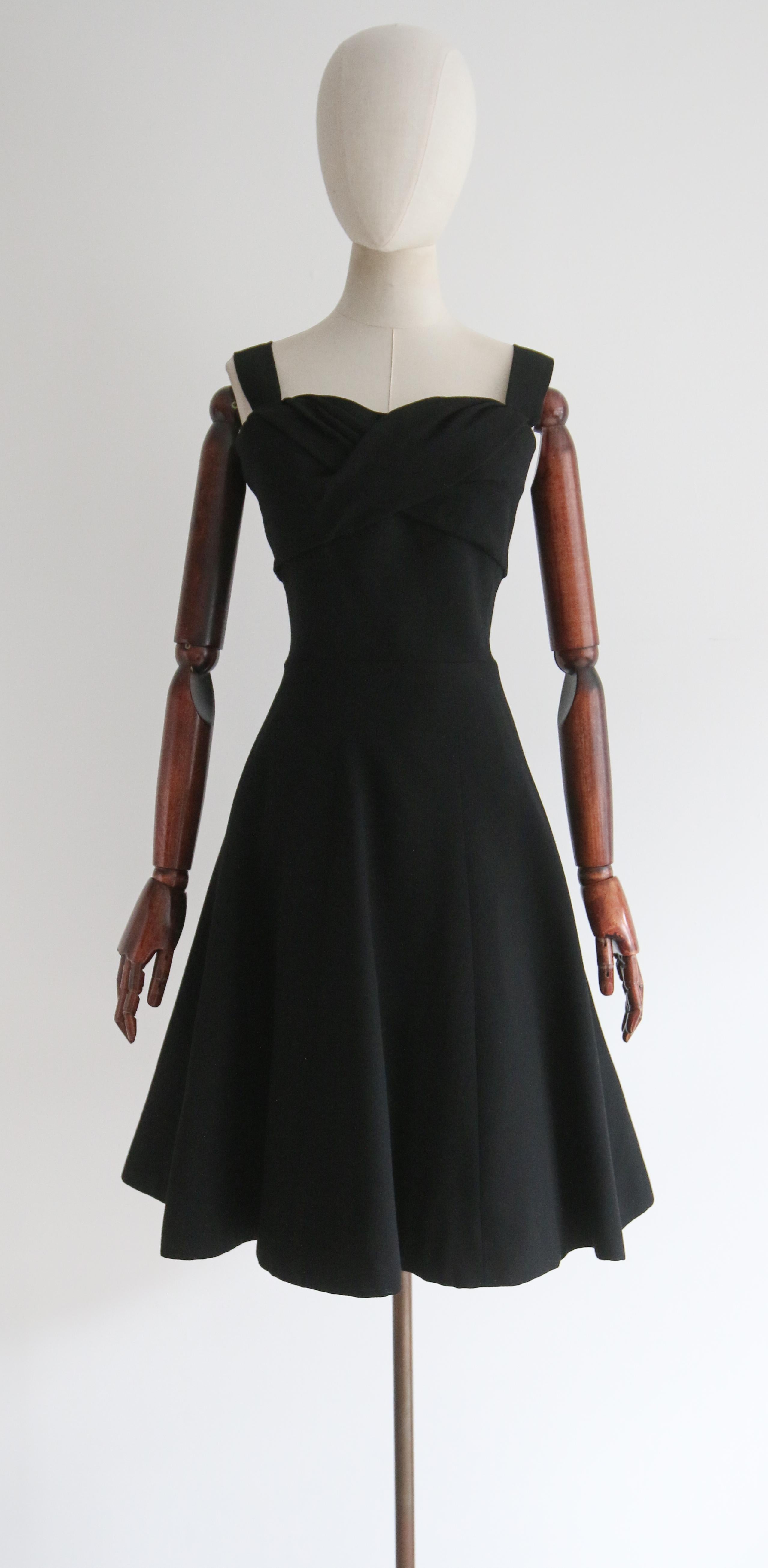 Dieses seltene Kleid von Christian Dior aus den späten 1950er Jahren aus tiefschwarzem Wollkrepp zeigt die ikonische Silhouette der Epoche und ist bis heute ein klassisches und zeitloses Design. 

Der runde, herzförmige Ausschnitt wird von breiten