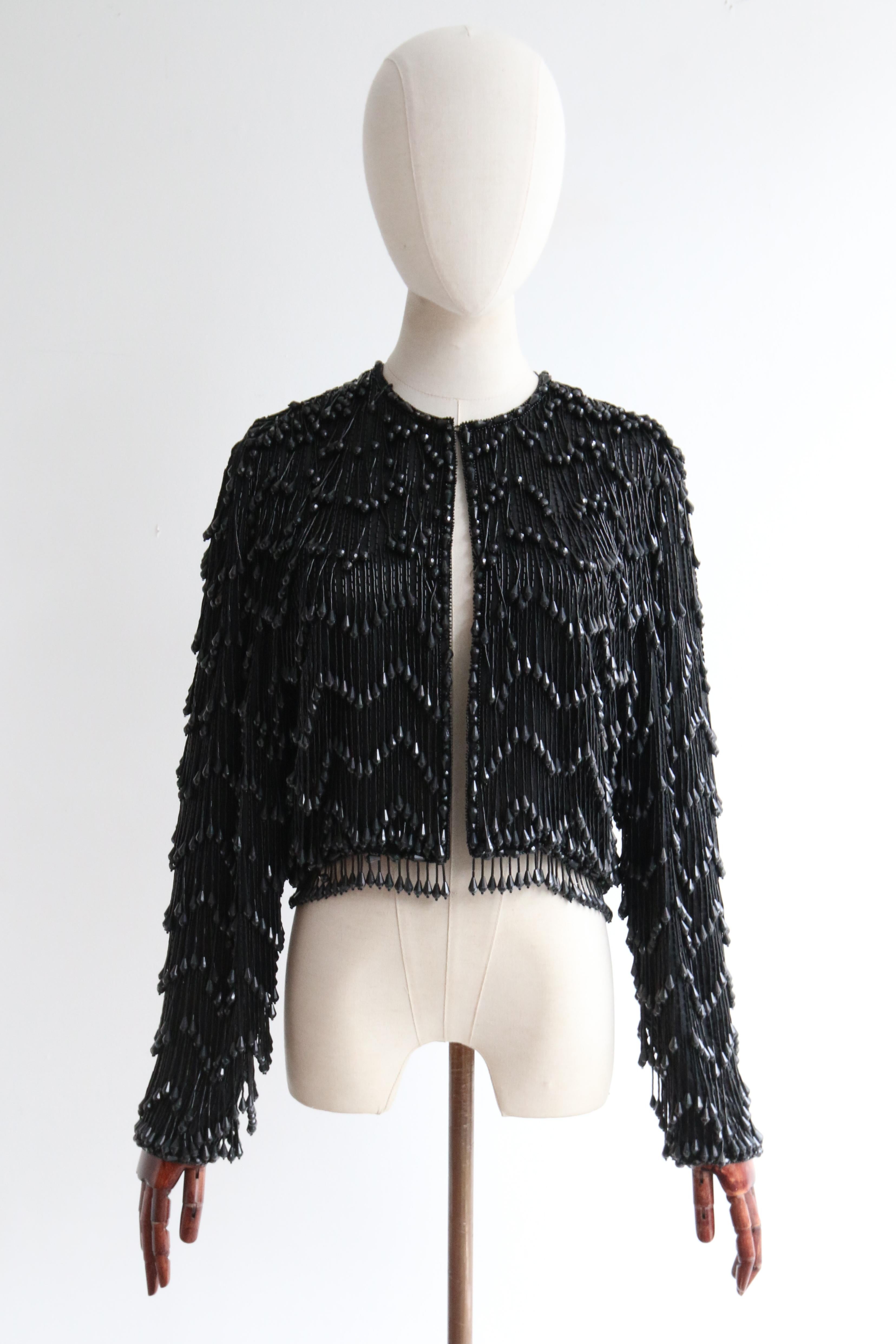 This truly mesmerising late 1960's silk chiffon based jacket by Victoria Royal LTD, fully embellished with black glass bugle beads sewn in horizontal stripes, beneath strands of black glass bugle beads finished with faceted teardrop beads in a