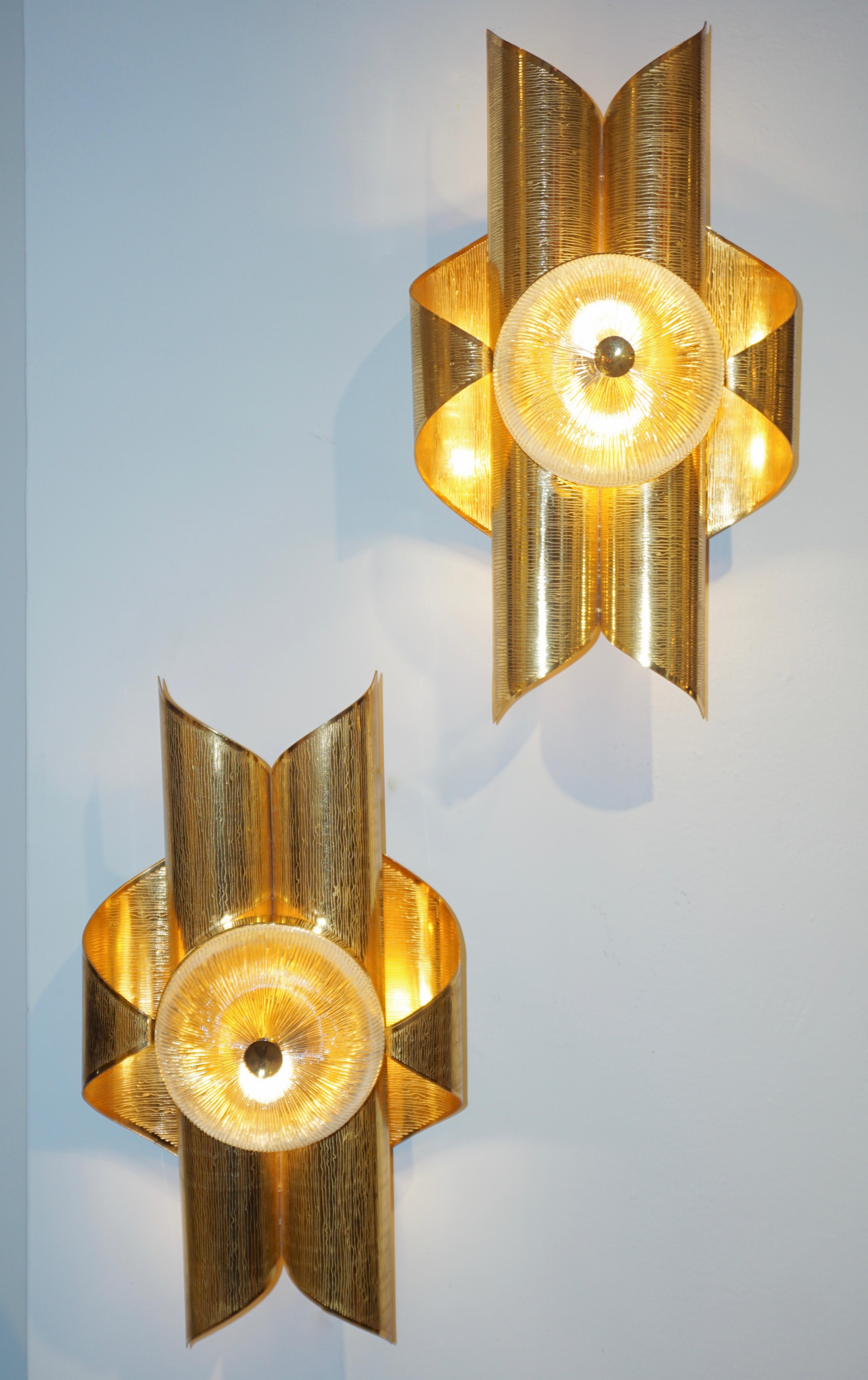 Mid-Century Modern French Hollywood Regency style wall lights, entirely handcrafted, with an Art Deco flair. The folded brass scrolled body has a curvaceous and sensuous design highlighted by a round crystal clear ribbed glass core that, when lit,