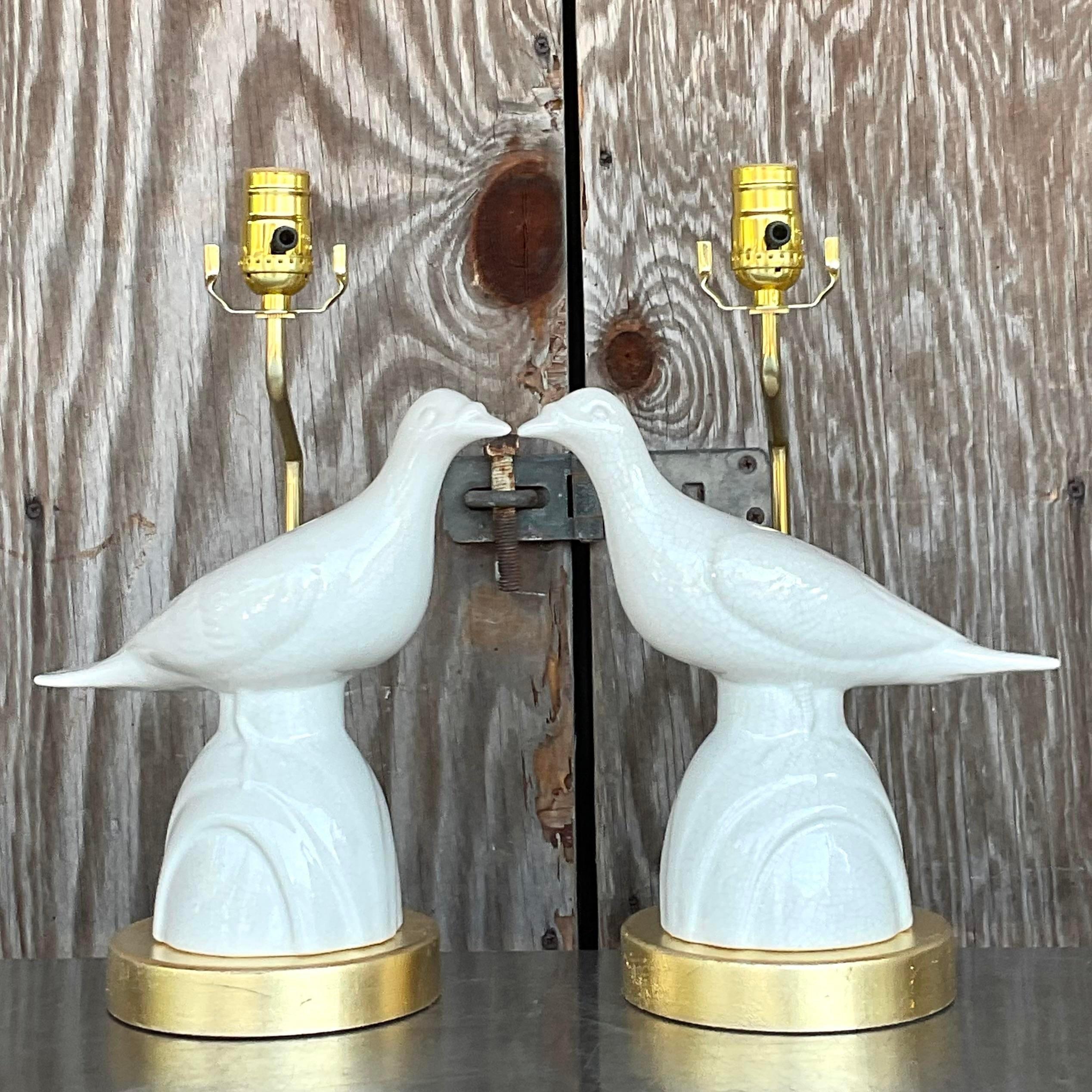 Une superbe paire de lampes de table Boho vintage. Magnifiques oiseaux d'amour en céramique émaillée ivoire reposant sur un socle doré. Entièrement restauré avec tous les nouveaux câblages, quincailleries et plinthes. Acquis d'une propriété de Palm