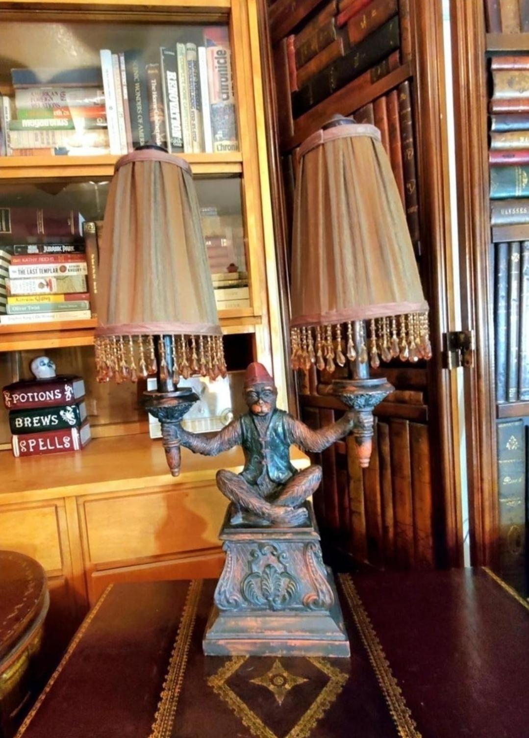 MAITLAND SMITH FIGURAL MONKEY LAMP.
The bellhop monkey is holding two urn form torches.
Beaded, ruched lampshades.
Ornately carved.
Light control is on the cord.
Height 25