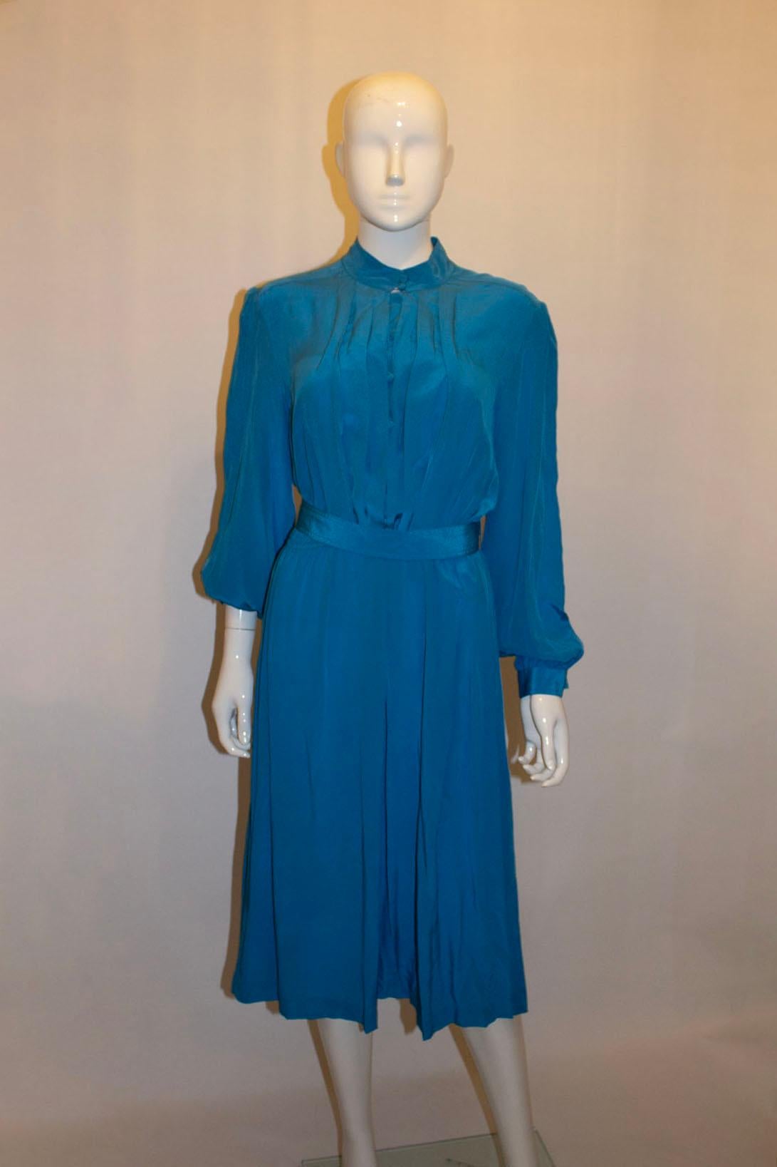 A vintage Laura Philips silk dress. In a pretty turquoise colour, the dress has a stand up collar, button front opening, folds/pleats at the front and an elasticated waist. It has two buttons cuffs, a self fabric belt and is unlined. Measurements: