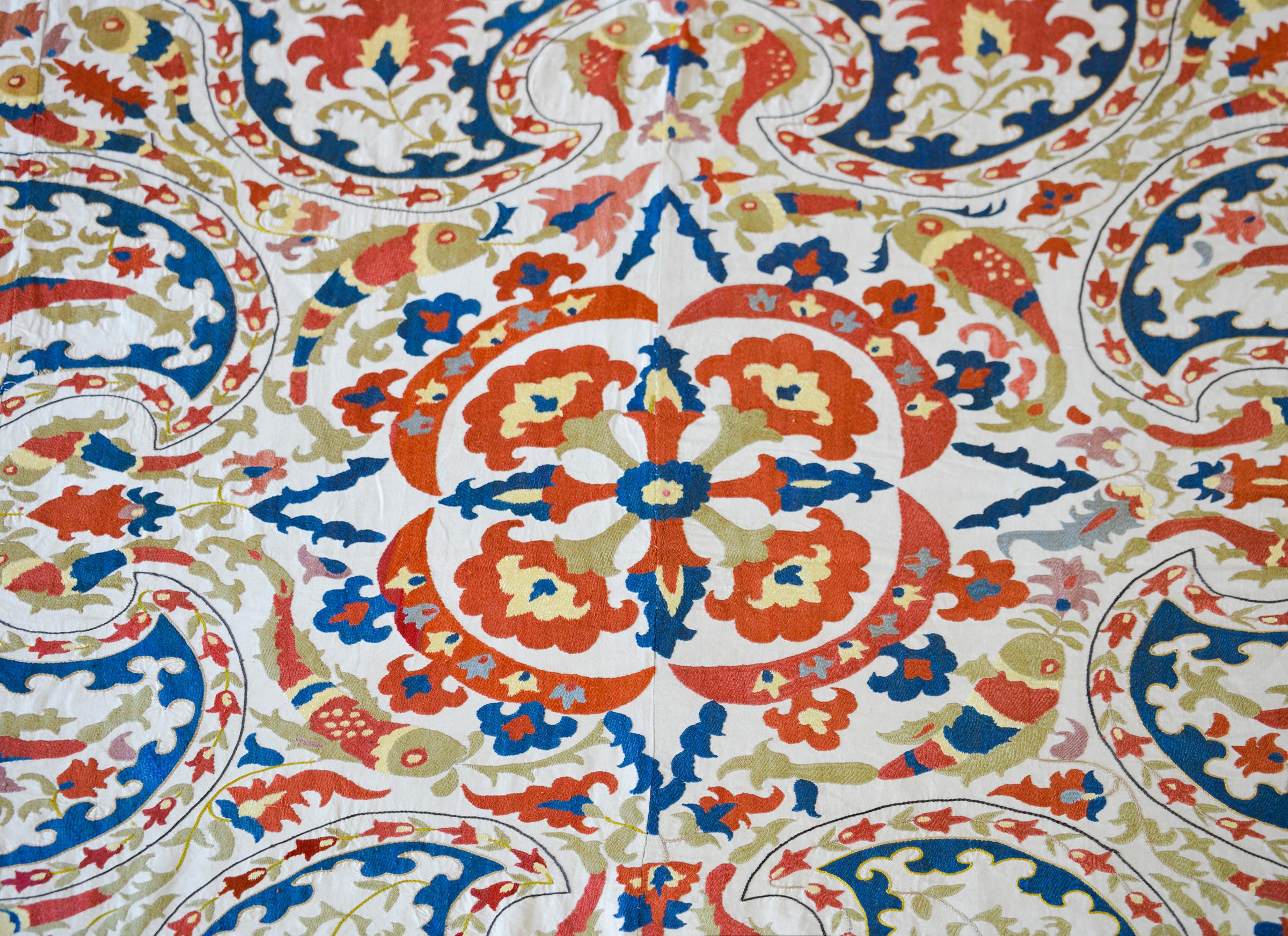 A striking vintage Uzbek Suzani with the most wonderful hand-embroidered pattern containing large-scale flowers, leaves, and vines, and myriad leaping fish, all woven in brilliant reds, golds, and blue silk thread, set against a white cotton backing.