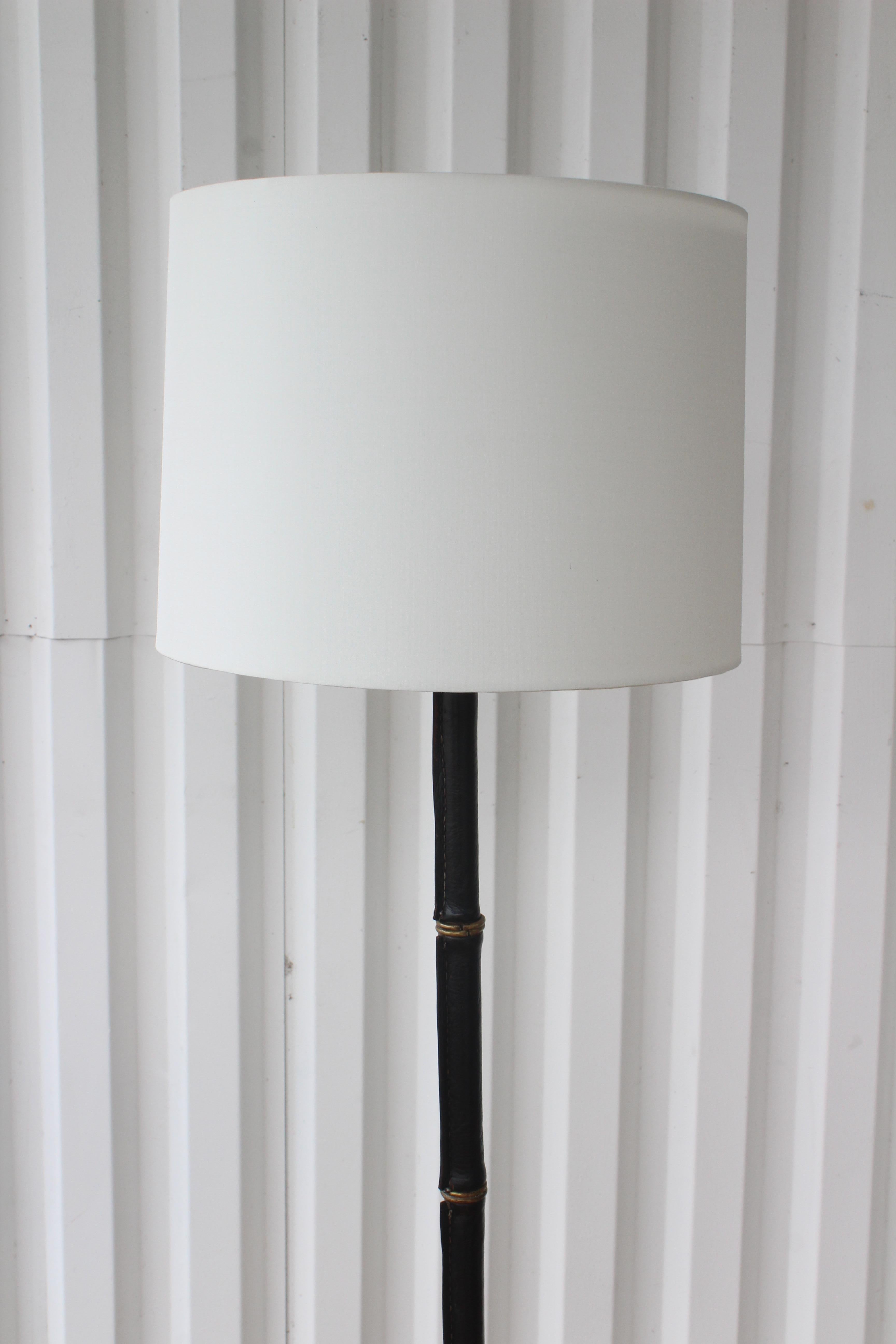 Vintage stitched leather floor lamp with brass accents by Jacques Adnet, made in France in the 1950s. The stitched black leather shows age appropriate wear but is in overall great condition considering the age of the piece. The brass ring accents