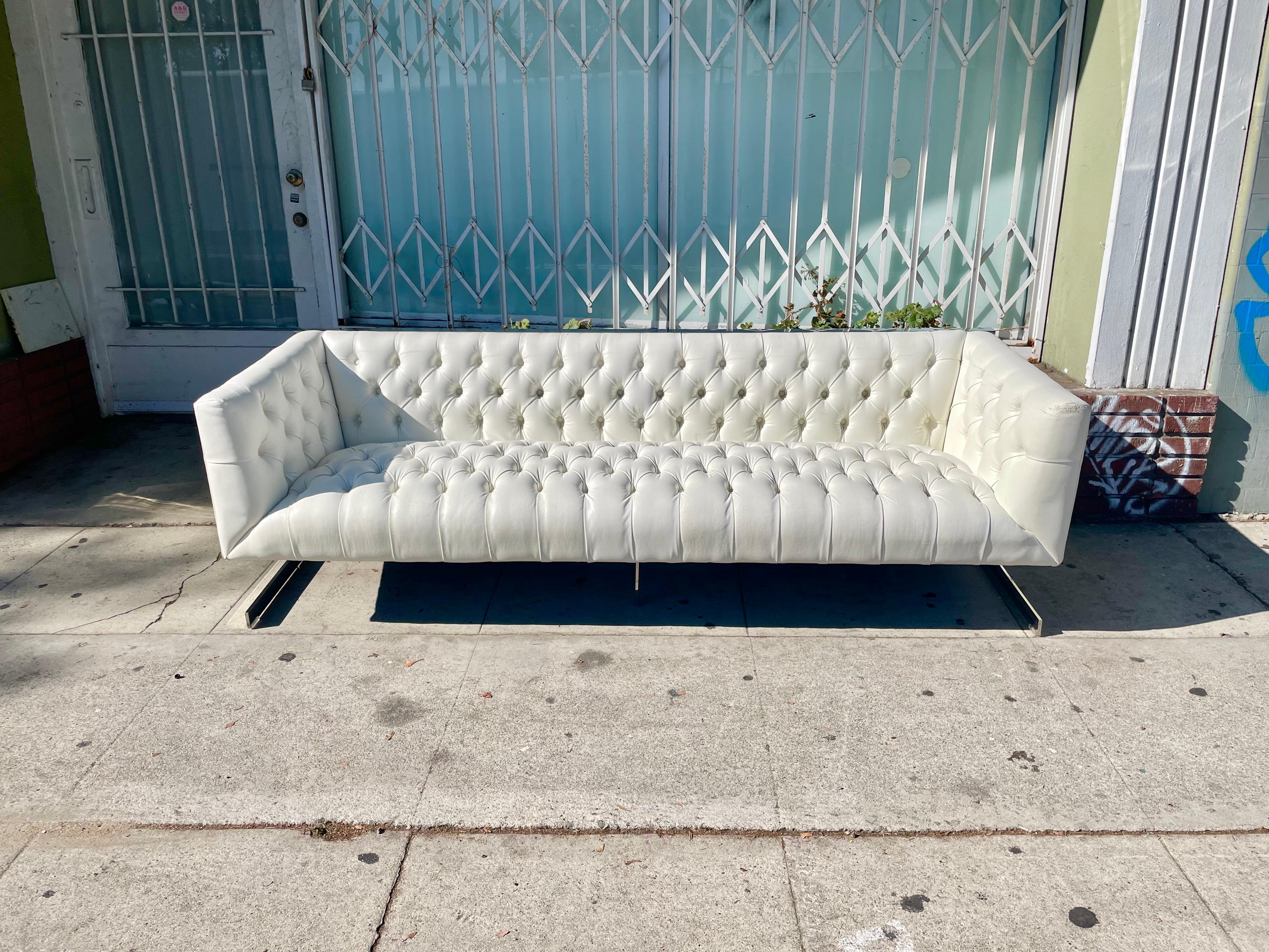 Vintage Leather and Chrome Chesterfield Sofa Styled After Milo Baughman was designed and manufactured in the United States circa 1970s. This beautiful sofa features a white leather upholstery that sits on top of a strong and sturdy pair of chrome