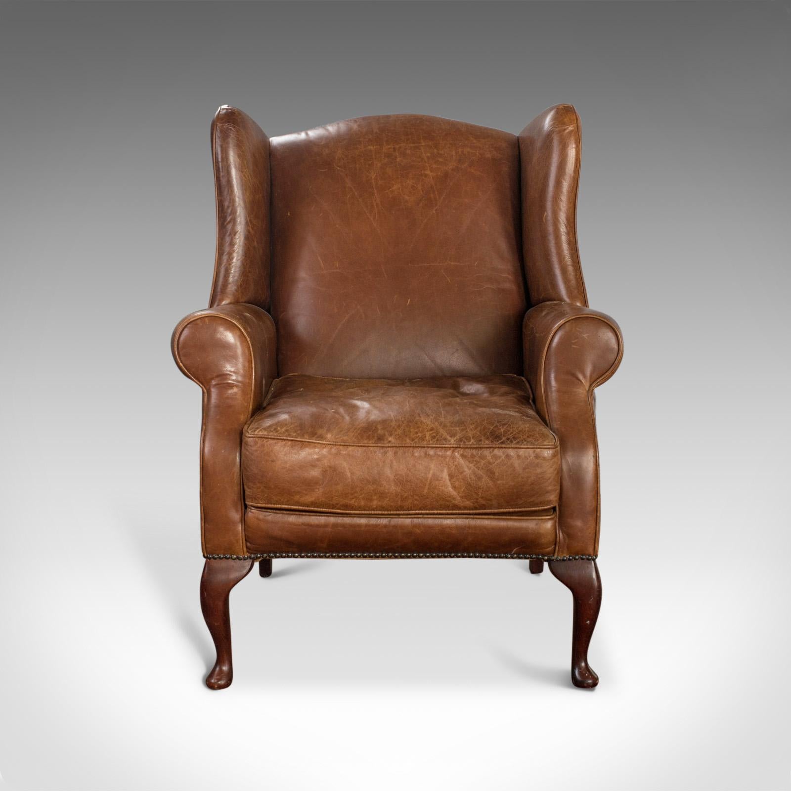 This is a vintage leather armchair. An English, saddle brown, wing-back chair dating to the late 20th century.

Richly colored leather displays a desirable patina
Piped seat cushion in good condition with no deterioration to the seams or