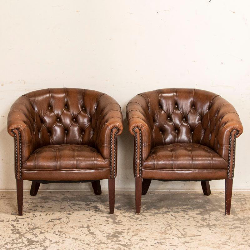 This pair of Chesterfield club chairs are in good condition for their age, with brown leather and buttons creating the tradition 