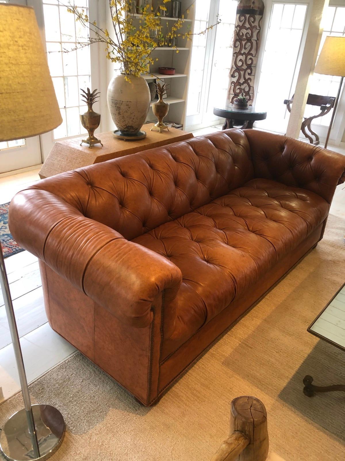 Classic 1970s Chesterfield sofa in rich caramel color leather. Sofa with large rolled arms and hardwood bun feet
Measures: Seat depth 24”.