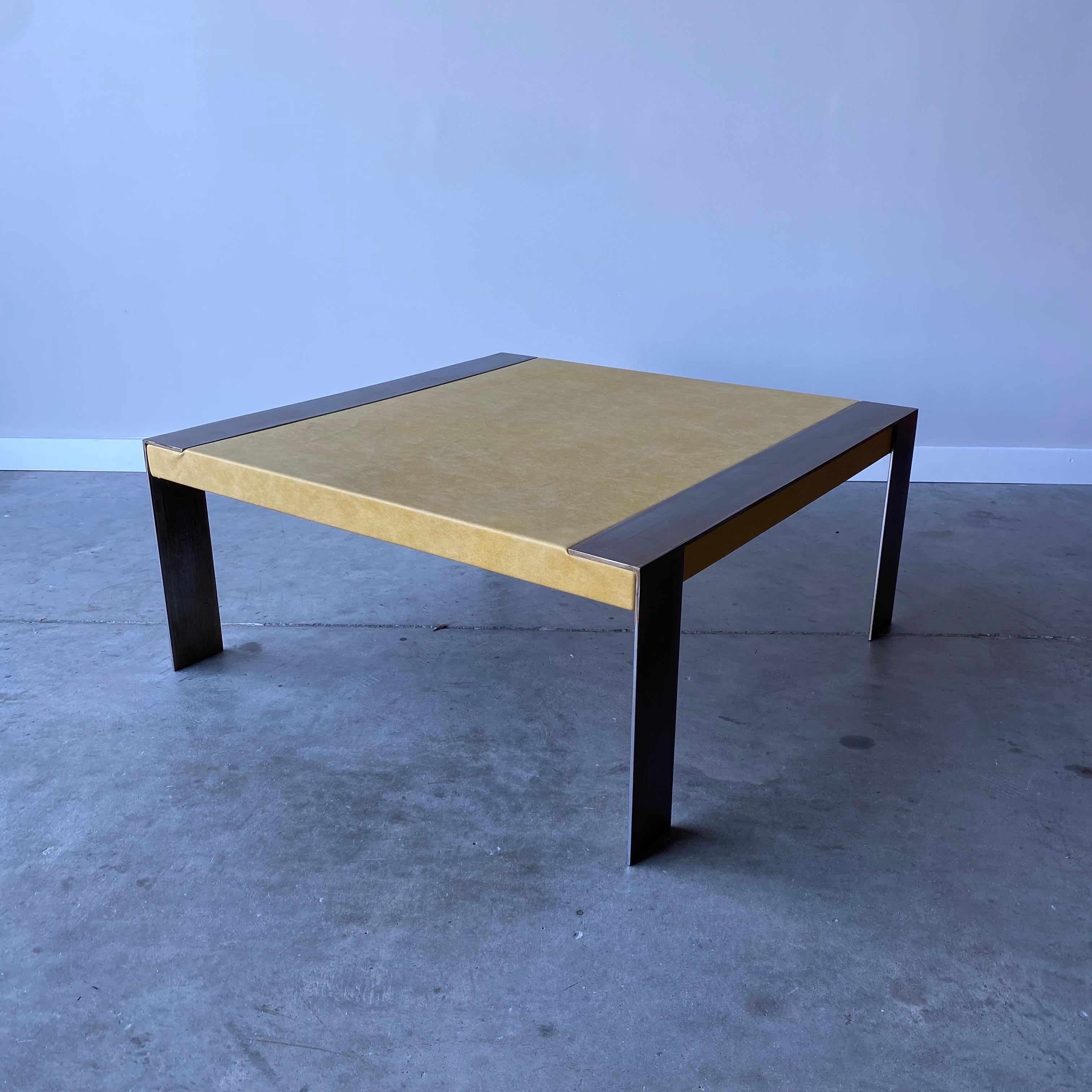 Une table basse unique avec un plateau en cuir et des pieds en acier patiné.  Élégant et industriel, avec une excellente combinaison de matériaux.