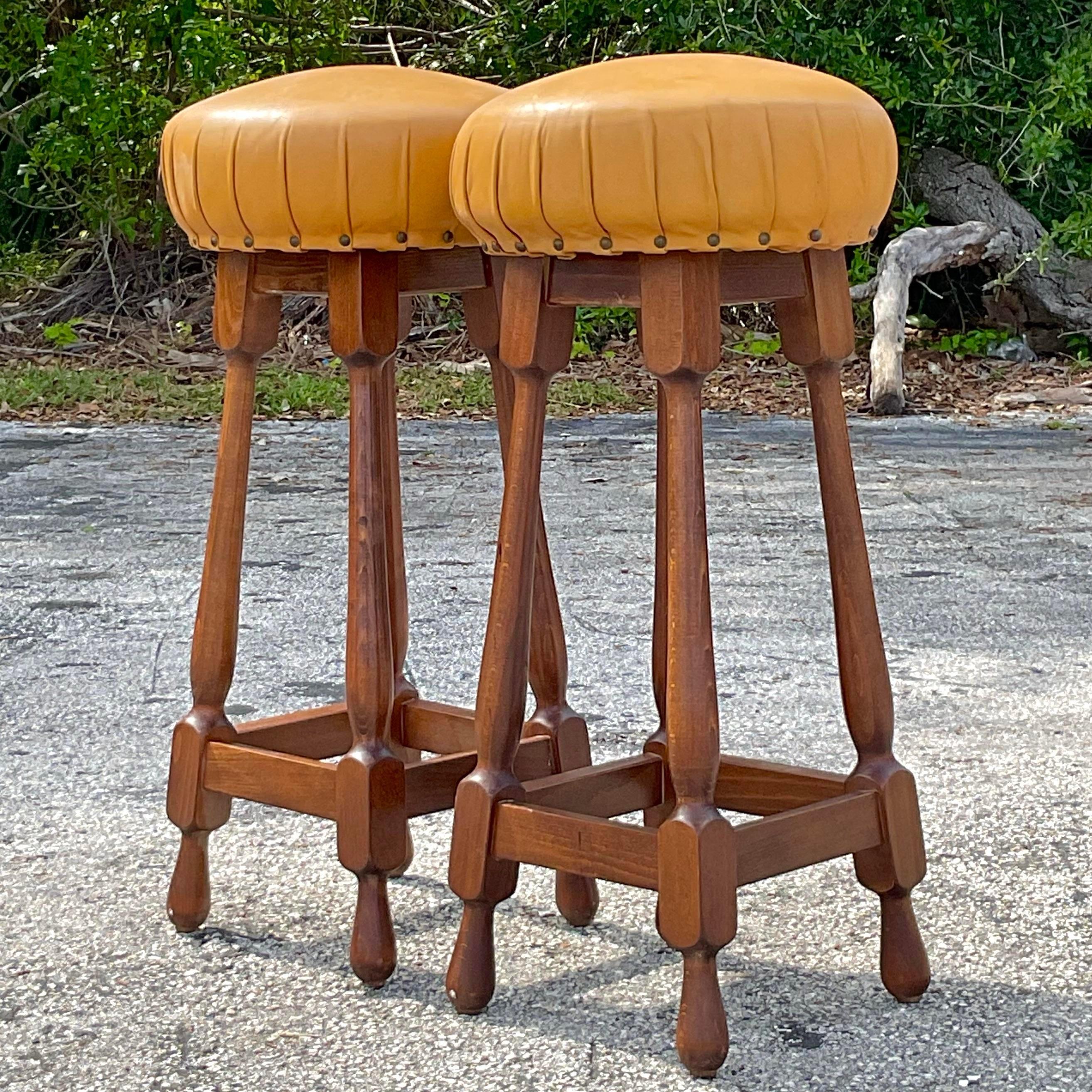 Incredible vintage old world barstools with leather seats that showcase a pleated pattern at their base with exposed nailheads. The spindle style base is intricately carved and sculptural. Great masculine addition to any old world bar or counter