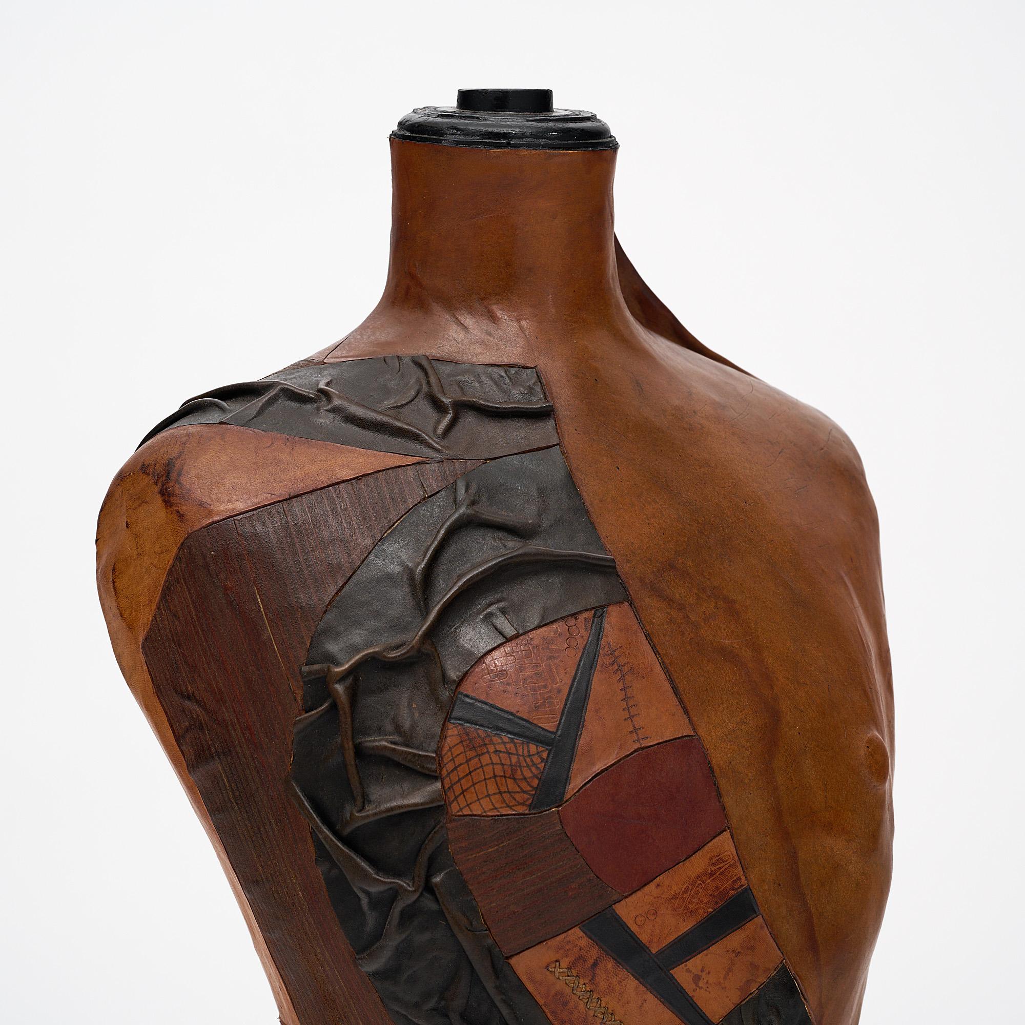Dress form mannequin that is covered with black and tan leather in freeform to imitate a man’s bust. The bust sits on a turned ebonized pear wood stand.