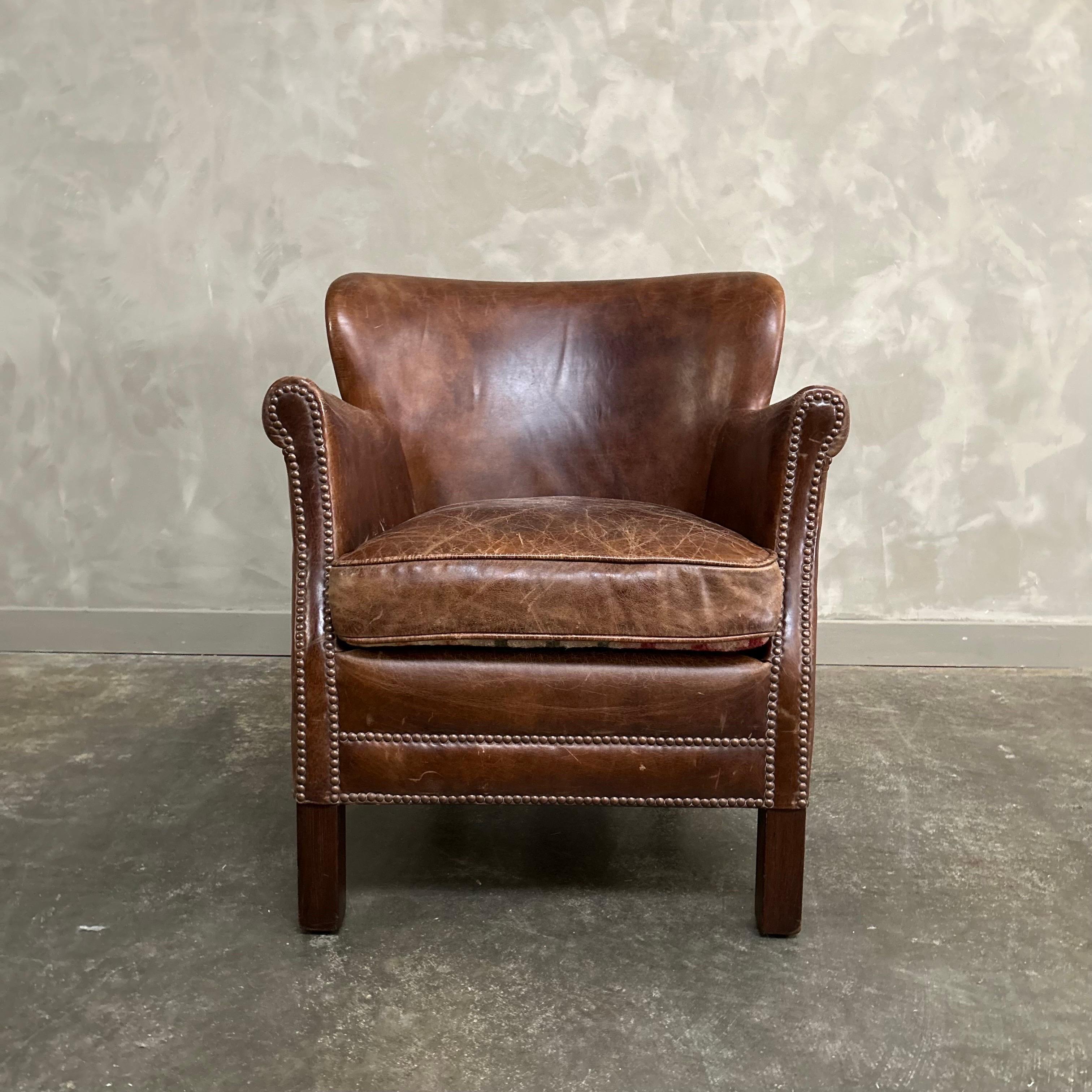 English leather club chair is small in stature, grand in style, this vintage chair provides all the presence and comfort of a larger chair. A 1920s English wing chair, its petite proportions and enveloping embrace offer seating on a more intimate