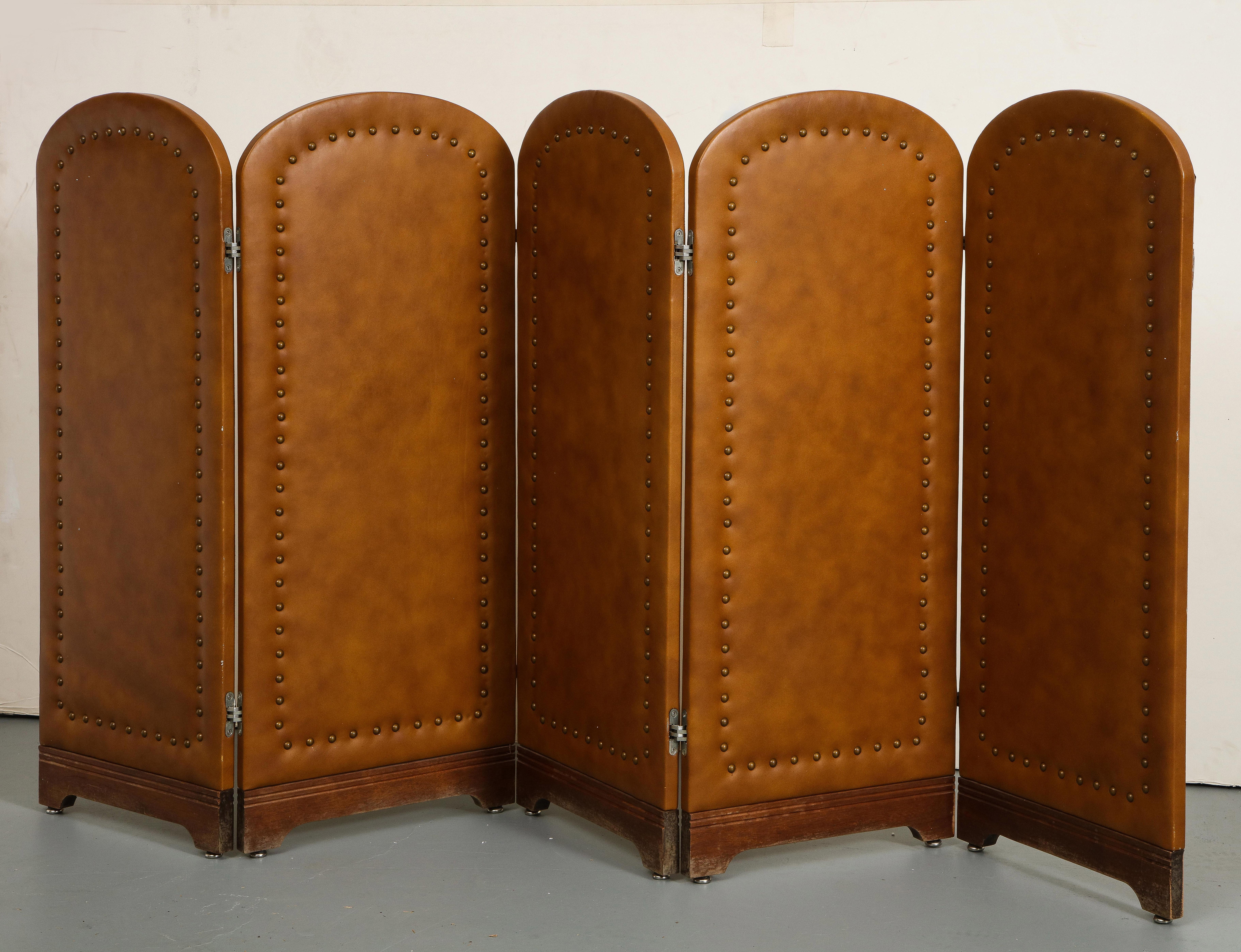 Vintage leather folding screen with 5 panels, c. 1960. Arched tops and brass nail head details on saddle brown leather over walnut frames. Silver metal feet on each panel. 

Each panel measures 16