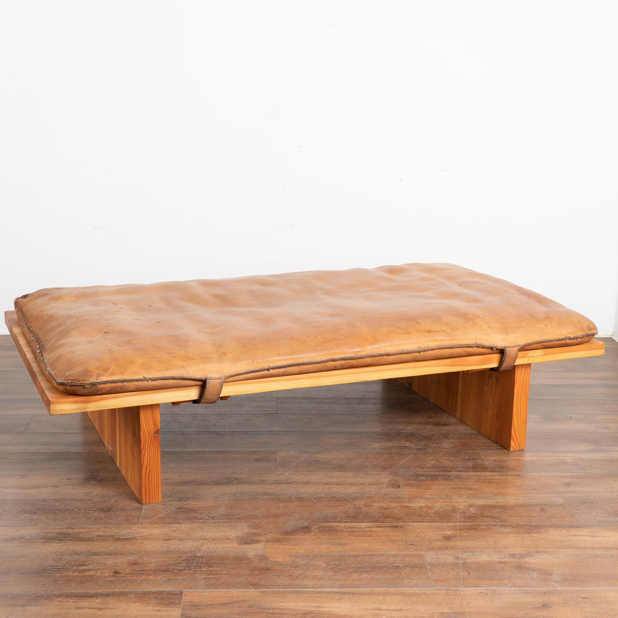 The vintage leather of this old gym mat is loaded with character and patina and rests on a wood base, creating an oversized ottoman or coffee table for today's modern home. 
The leather reveals stains, scuffs/scratches from years of use, and will