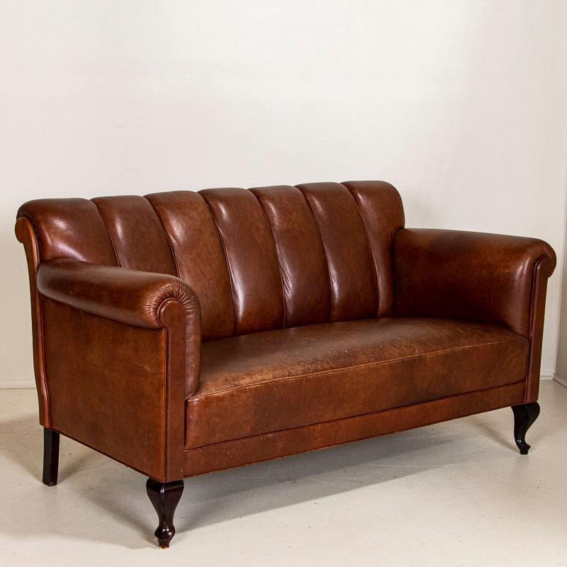 This handsome loveseat and pair of small scale barrel back club chairs are a great find for one searching for an authentic vintage leather set. The rich brown leather is accented with piping and cabriolet legs. While there are minor/expected scuffs