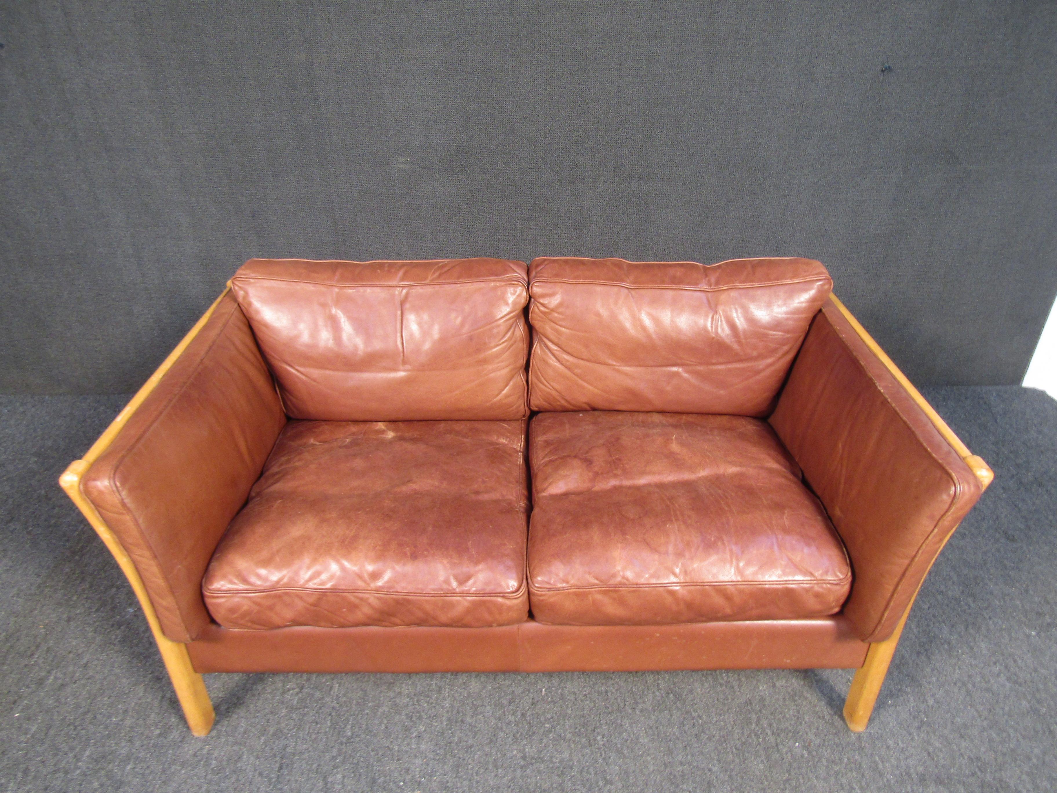 Combining leather upholstery with wooden frames, this vintage couch offers comfortable seating through a stylish Mid-Century Modern design. Please confirm item location with seller (NY/NJ).