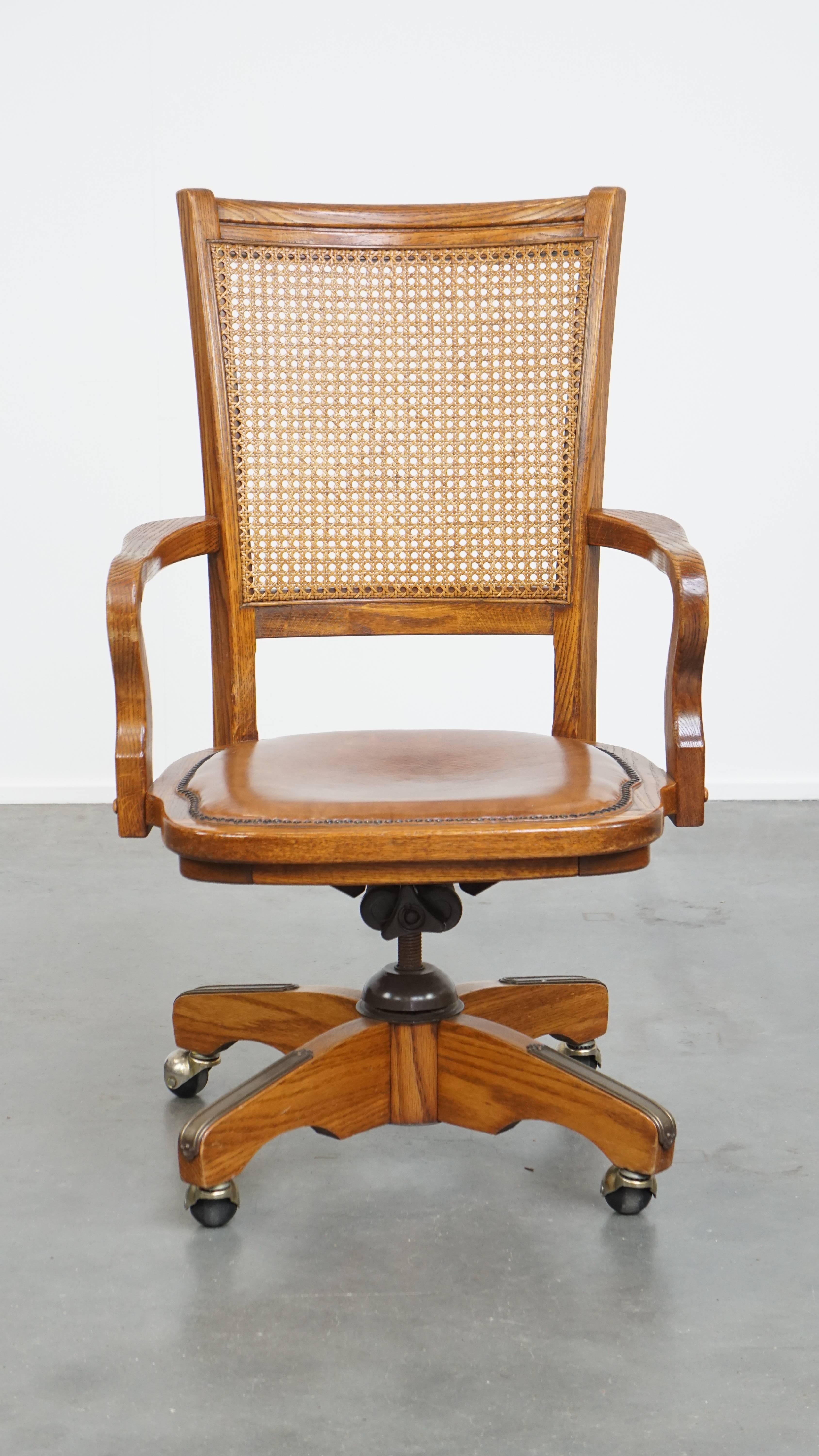 Angeboten wird dieser luxuriöse cognacfarbene Vintage-Bürostuhl auf Rollen mit einem Holzrahmen und einer Rückenlehne aus geflochtenem Schilfrohr.

Dieser auffällige Stuhl kombiniert eine Holzstruktur, einen Ledersitz und eine Rückenlehne aus