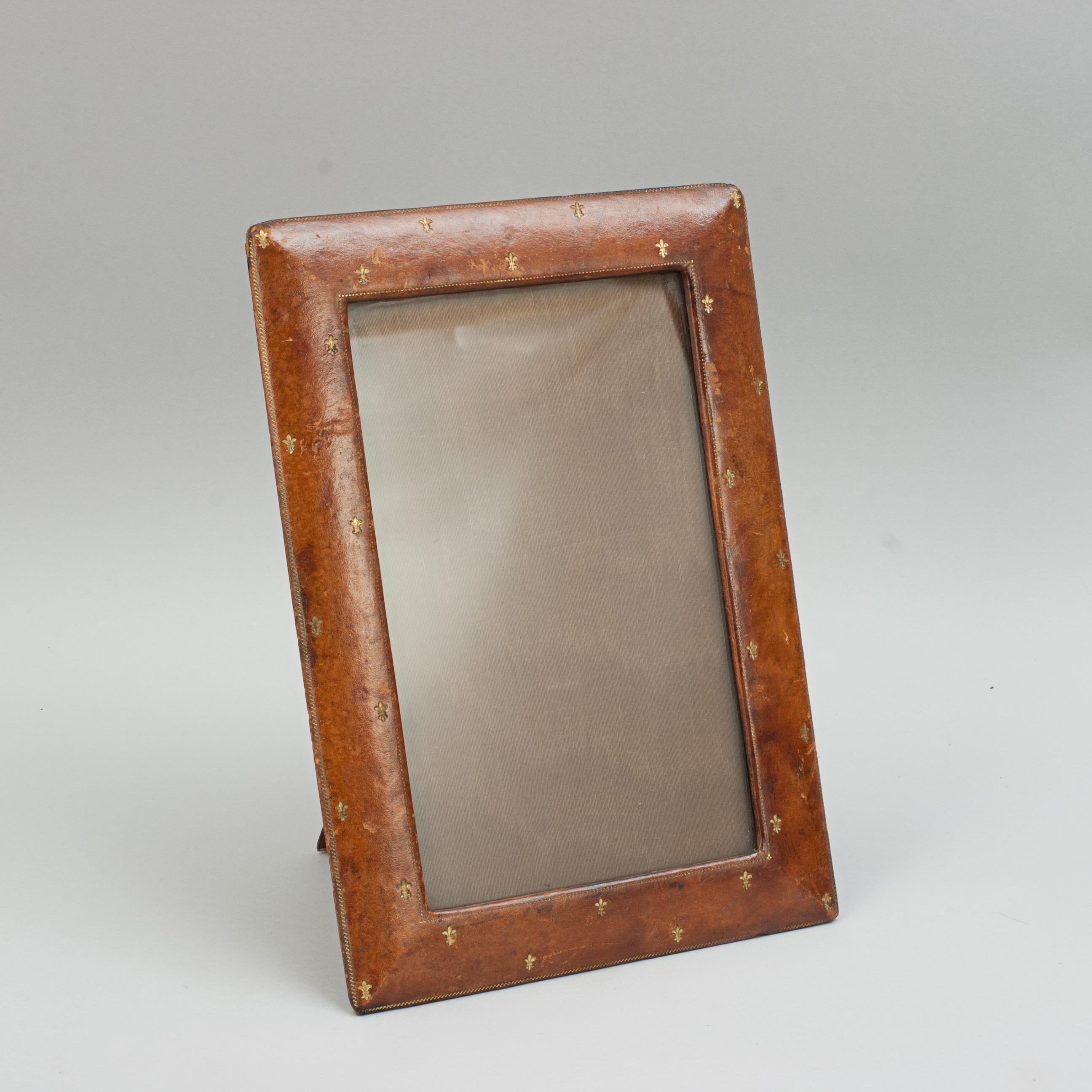 Vintage rectangular leather photo frame.
A tan leather photo frame, portrait style, with an extendable support leg to the rear. The frame with gilt decoration of embossed fleur-de-lis (also spelled fleur-de-lys). The aperture size is 9