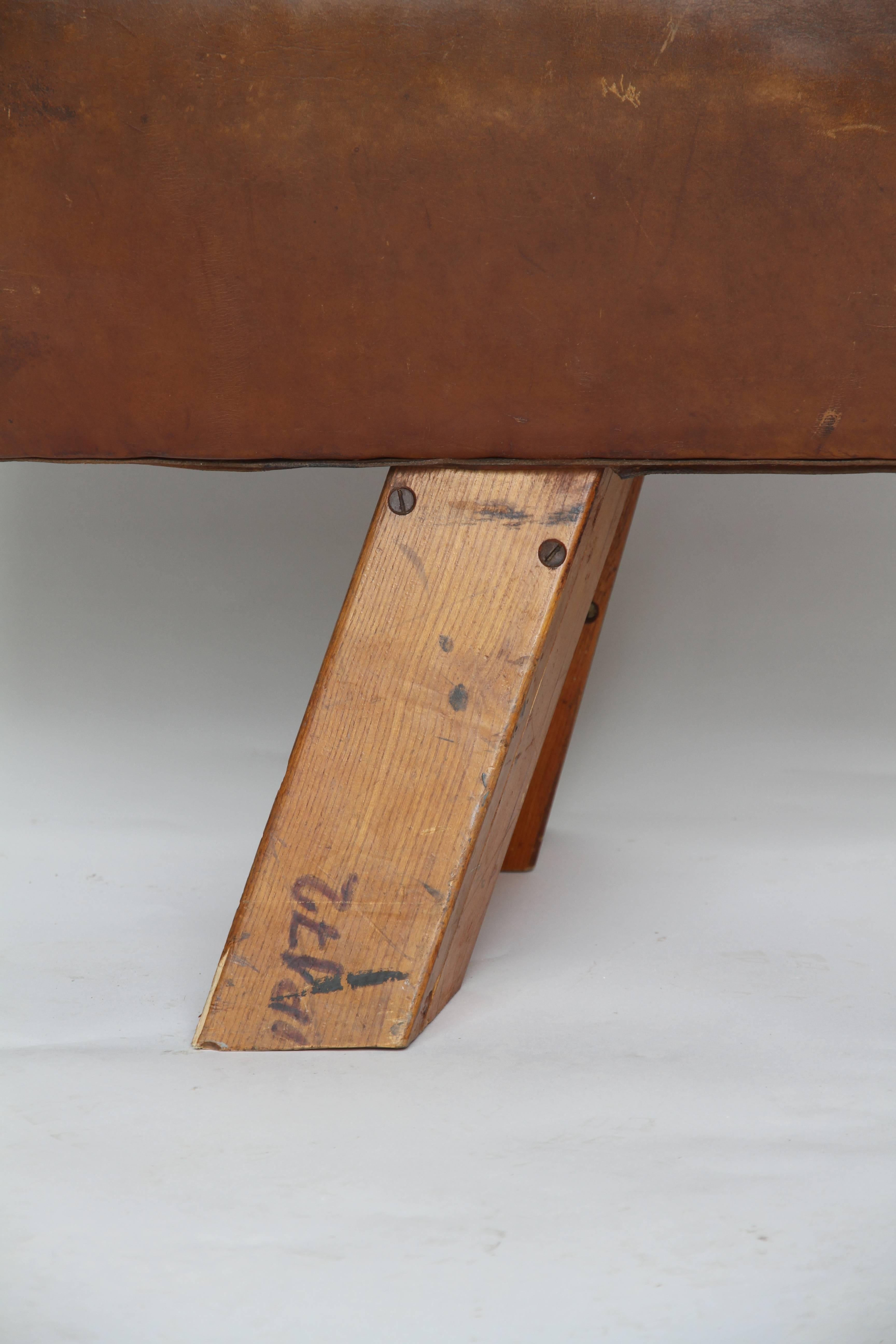A handsome leather pommel horse found in France. Probably from the 1950s, the wood legs have been shortened and metal plates cover the location of the original handles creating a unique bench. The piece is in nice condition with no cracks or tears