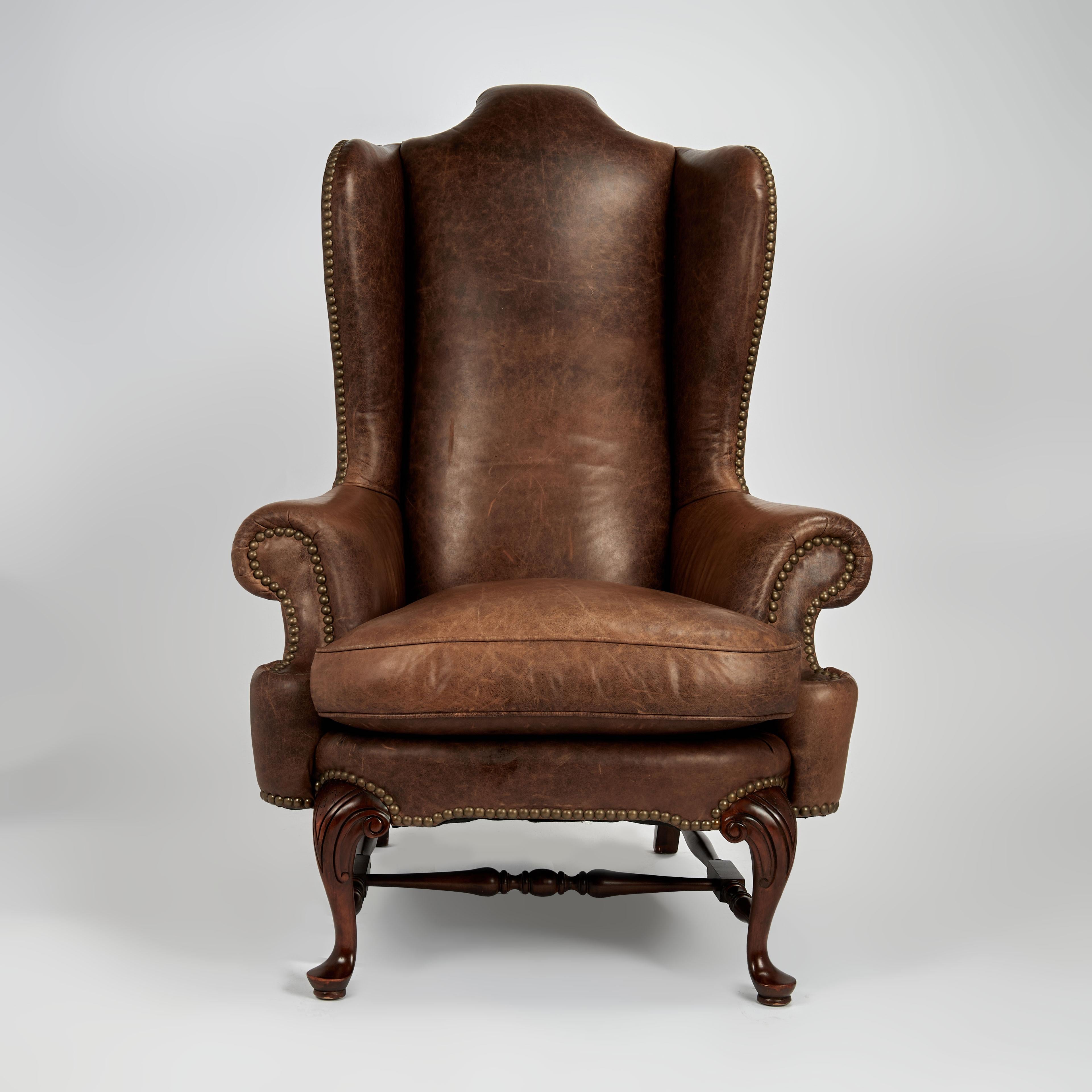 Splendida poltrona wingback d'epoca rivestita in lussuosa pelle marrone, dalla classica forma Queen Anne con puntine in ottone e poggiata su gambe cabriole intagliate. Firmato Beacon Hill sotto il cuscino.