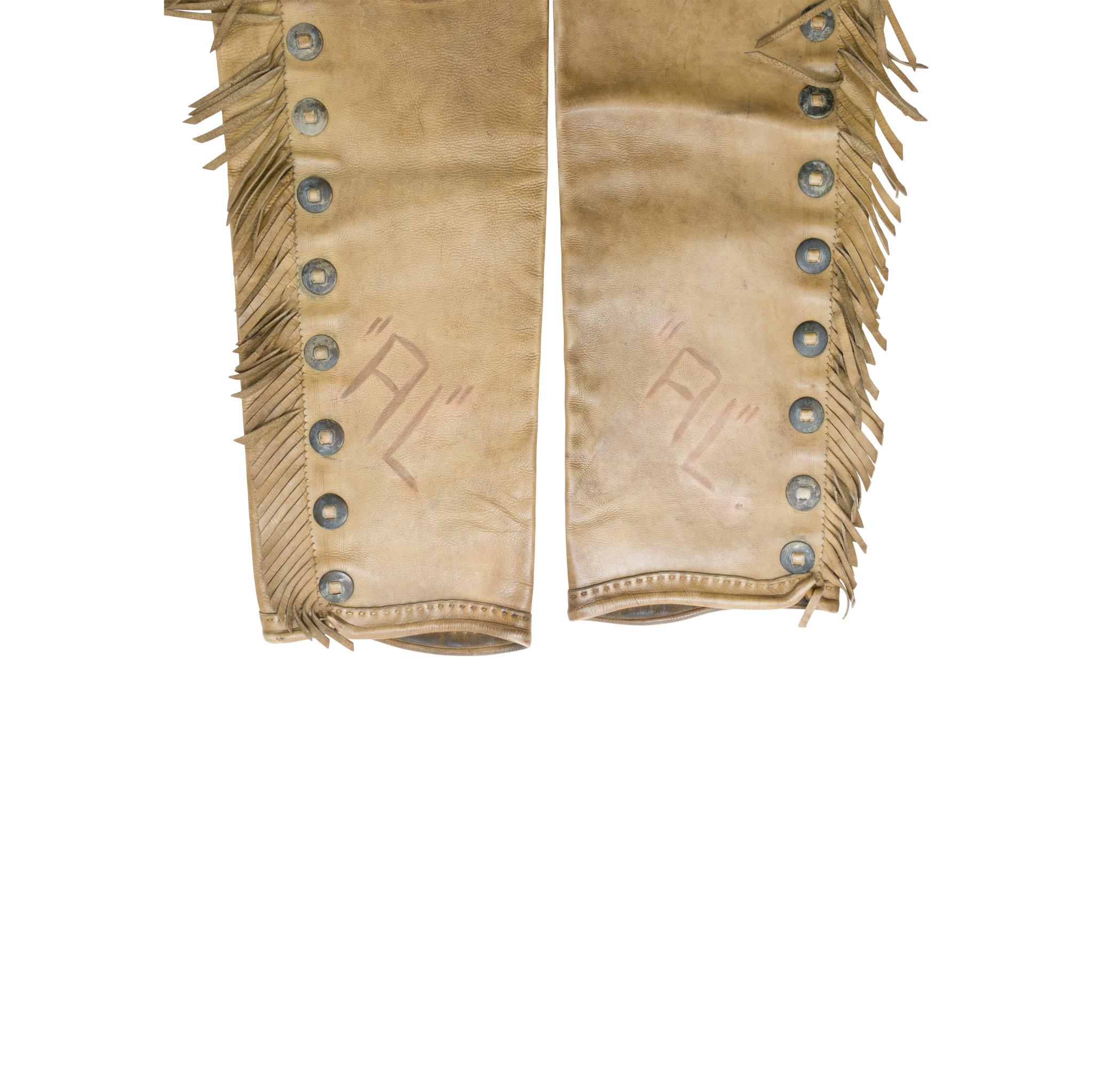 Vintage leather R.T. Frazier shotgun chaps with outside buck stitched pockets, fringe and conchos. Assume owner's initials or brand 