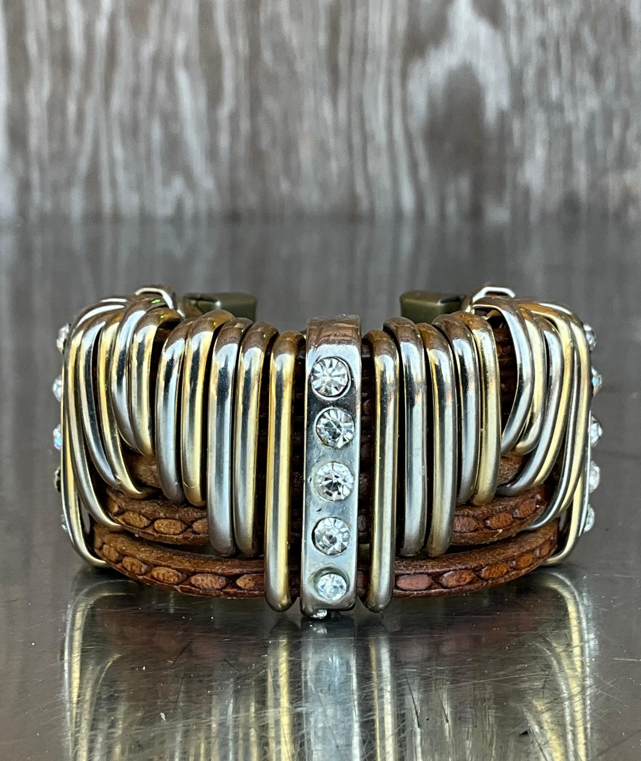 Questo bracciale vintage in pelle e strass d'argento è un pezzo straordinario che unisce il fascino rustico al fascino vintage. Realizzato in vera pelle invecchiata, l'ampio polsino emana un fascino robusto e vissuto, ammorbidito dal delicato