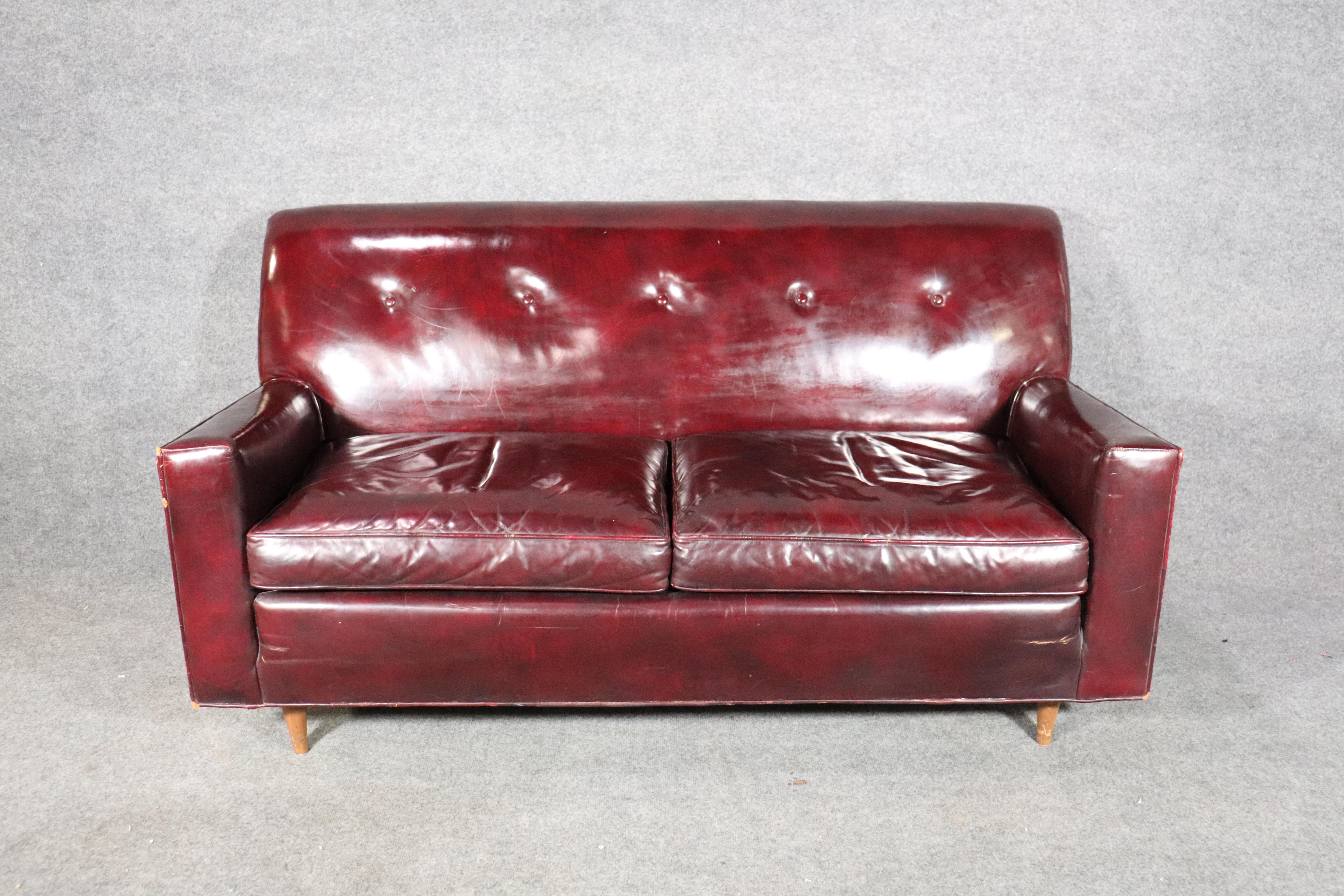 Well worn burgundy leather sofa with tufted back and tapered wood legs.
Please confirm location.