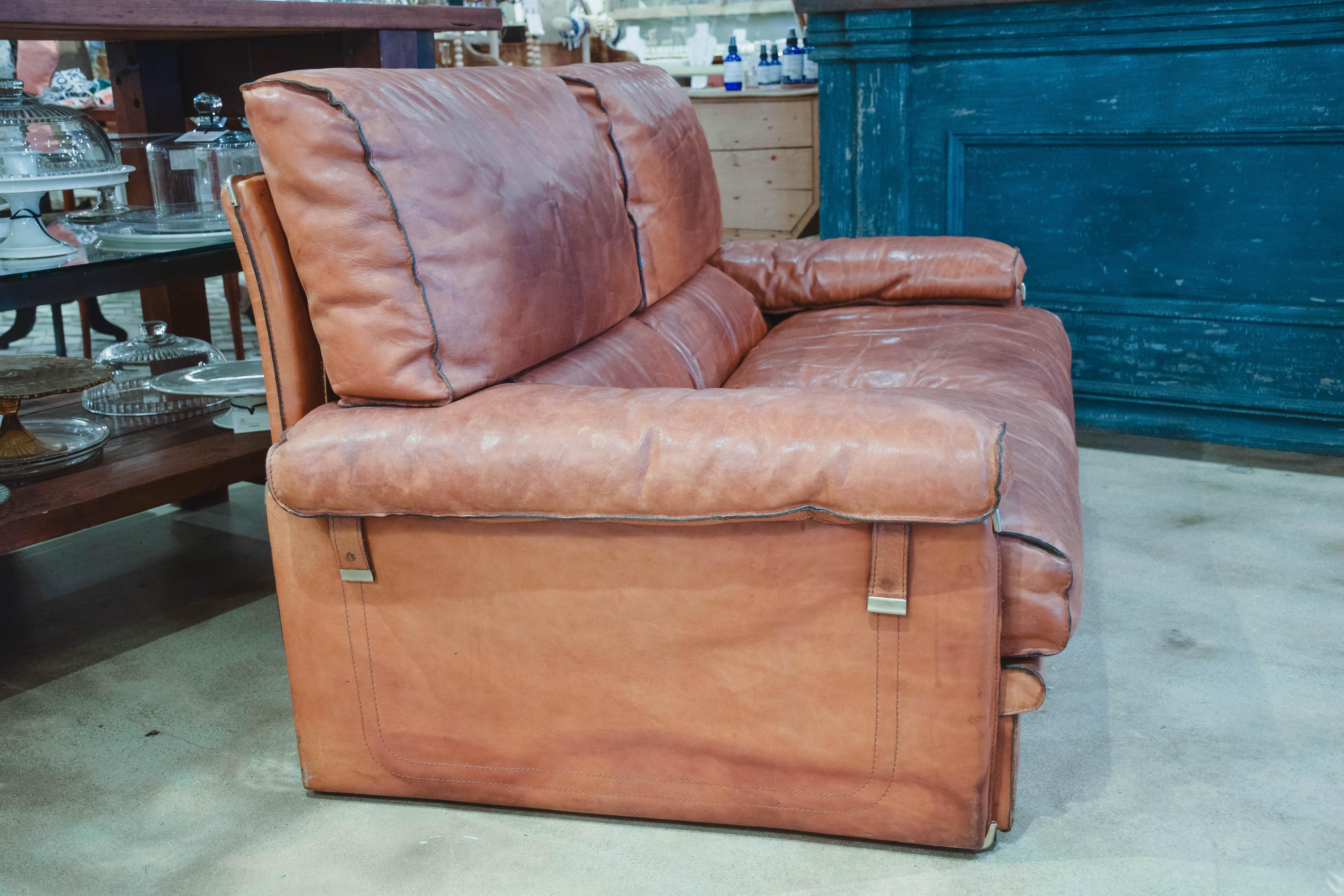 This is a wonderful and comfortable leather sofa in the style of Arcon. The large and comfortable sofa was created in 1970 in leather and offers a beautiful aged patina. The heavy wrapped leather frame shelters soft seats and back cushions, all with