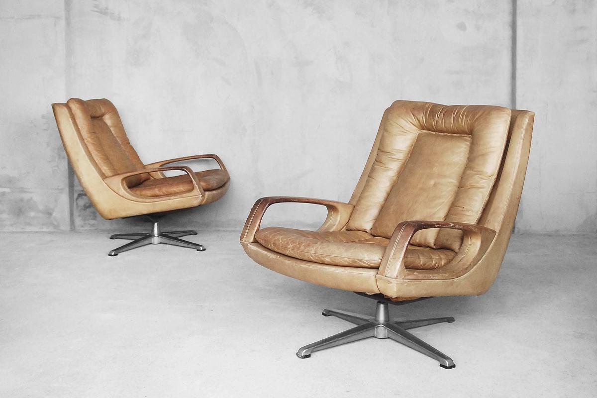This pair of leather lounge armchair was created by Carl Straub during the 1950s. This swivel chairs are upholstered in coffee late brown leather with natural patina. The armchair stands on a metal swivel base. The frame and armrests are made from