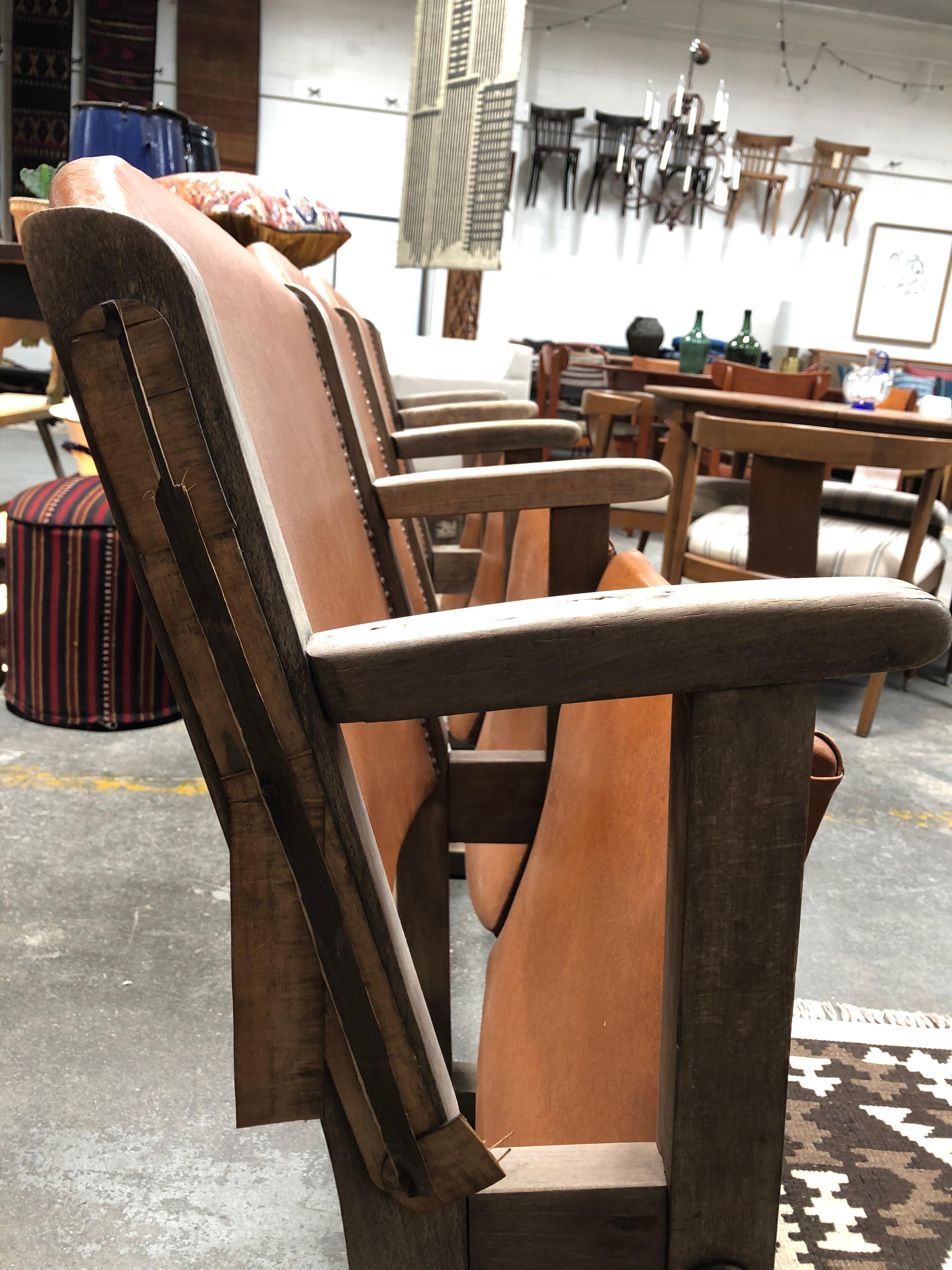 Caramel colored leather theater seats. Accented with studding along the leather seat back and set in wooden seat frames. All four chairs connected through wooden frame, in working condition, and set in soft leather. 

Dimensions of chairs:

Seat
