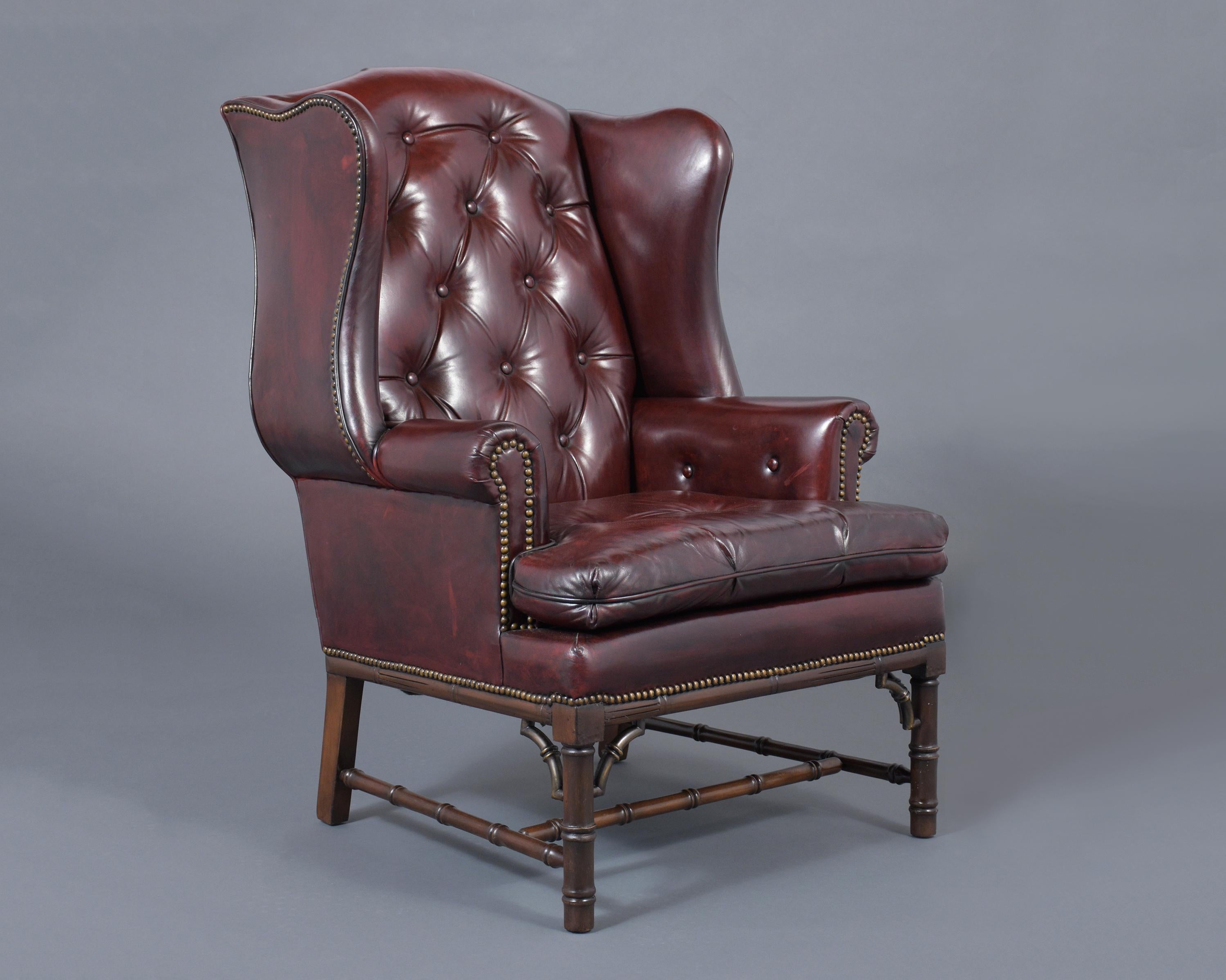 A 1970's wingback chair and ottoman has been professionally restored and handcrafted out of mahogany wood and features a leather upholstery tufted design with brass nailheads trim details, has been newly dyed in a dark burgundy color and waxed &
