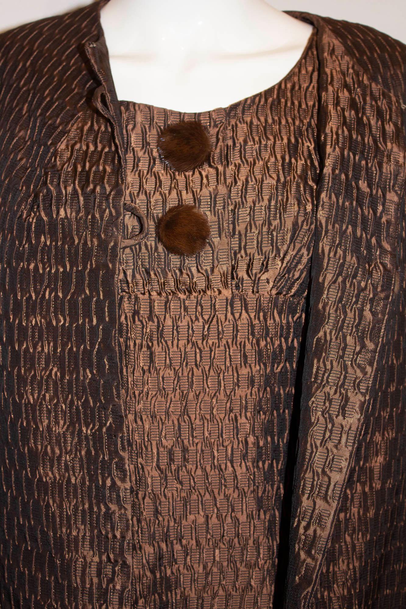 Un ensemble manteau et robe vintage chic par Lee Delman. En tissu texturé de couleur bronze/brun. La robe a une encolure ronde, avec 2 boutons sur le devant, une fermeture éclair centrale au dos et est entièrement doublée. Le manteau  a une encolure