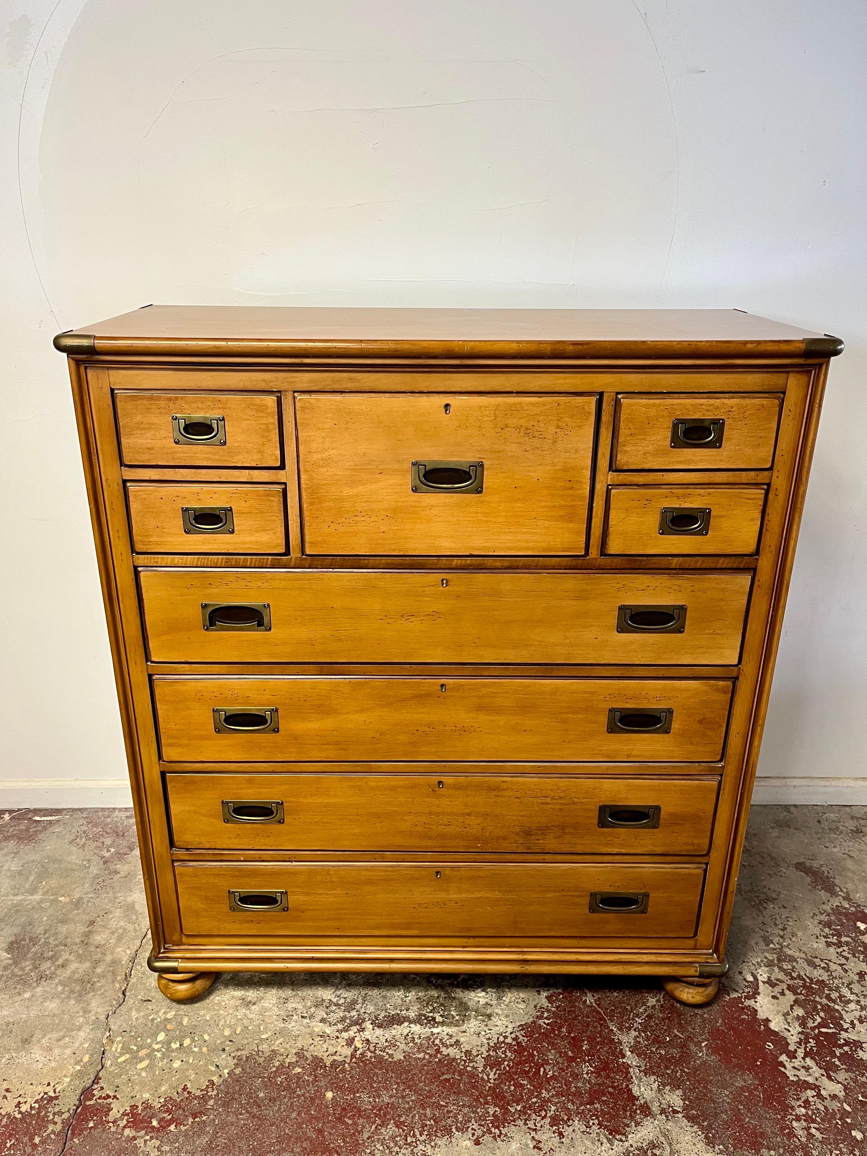 A light stained wood dresser with brass accents by Lexington Furniture Nautica Home Collection. The chest features ample storage, 9 drawer, with brass handles, Brass capped corners and bun feet. The inside of the top right drawer reads “Nautica