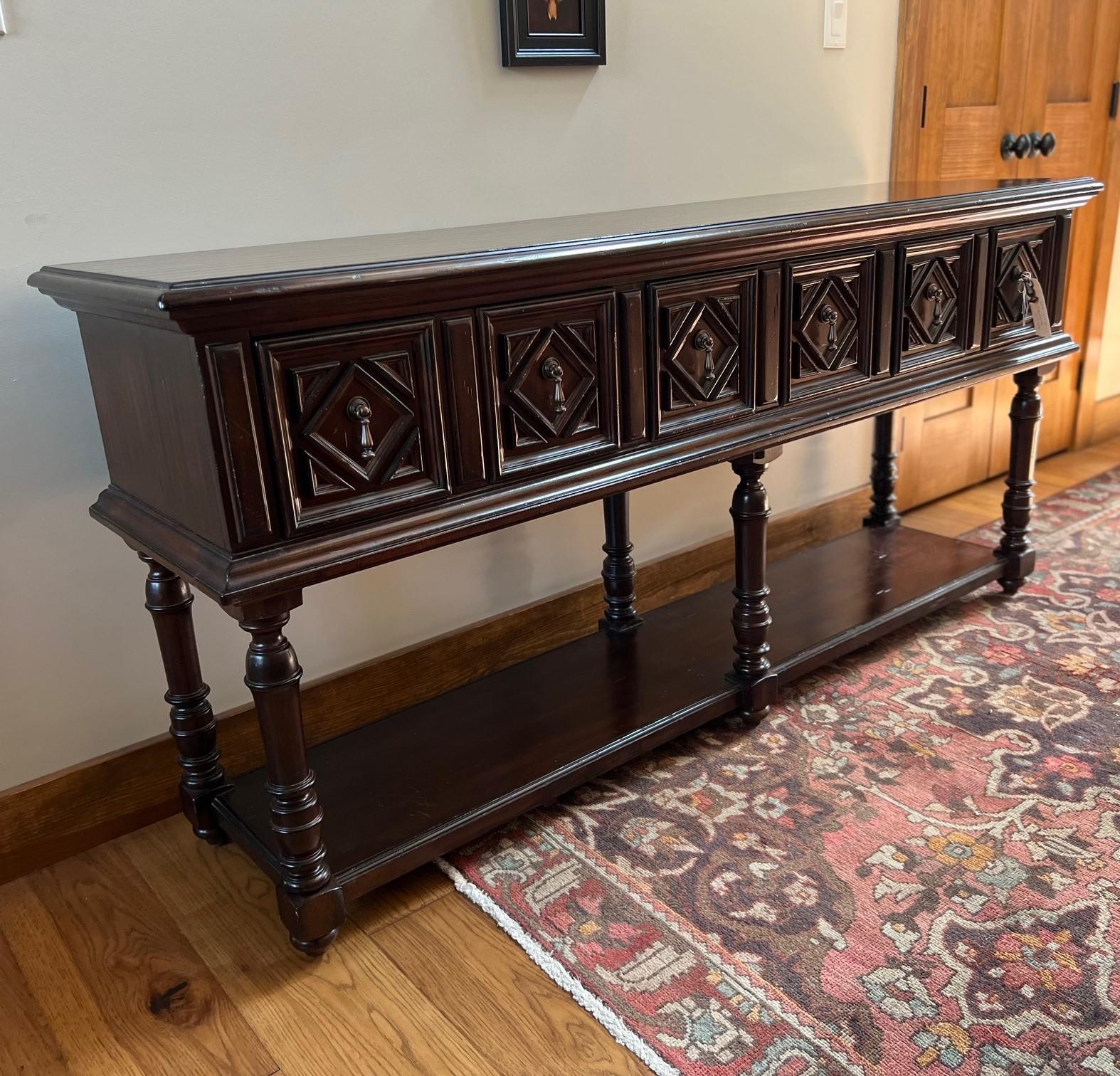 20th c. vintage console by Lexington Furniture, a well-known American furniture manufacturer. Made of solid wood, likely walnut, with a rich, dark finish that highlights the natural grain of the wood. The front features a series of carved panels,