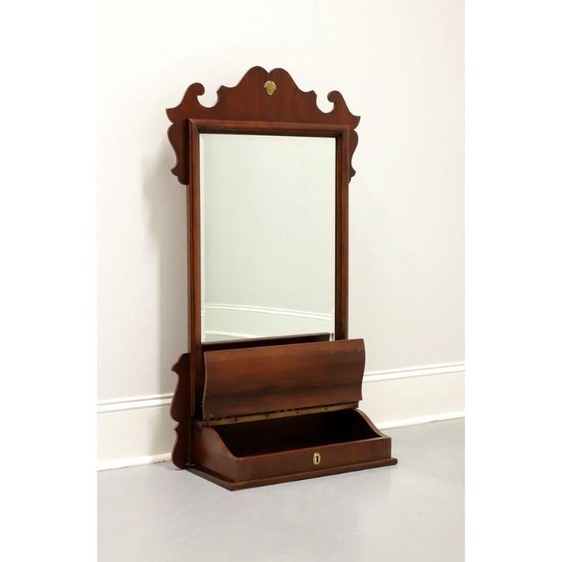 A Chippendale style dressing table mirror by Lexington Furniture. Beveled mirrored glass, portrait oriented, decoratively carved mahogany frame with gold shell ornamentation. Drawer base for storage with lifting scroll lid and brass faux keyhole