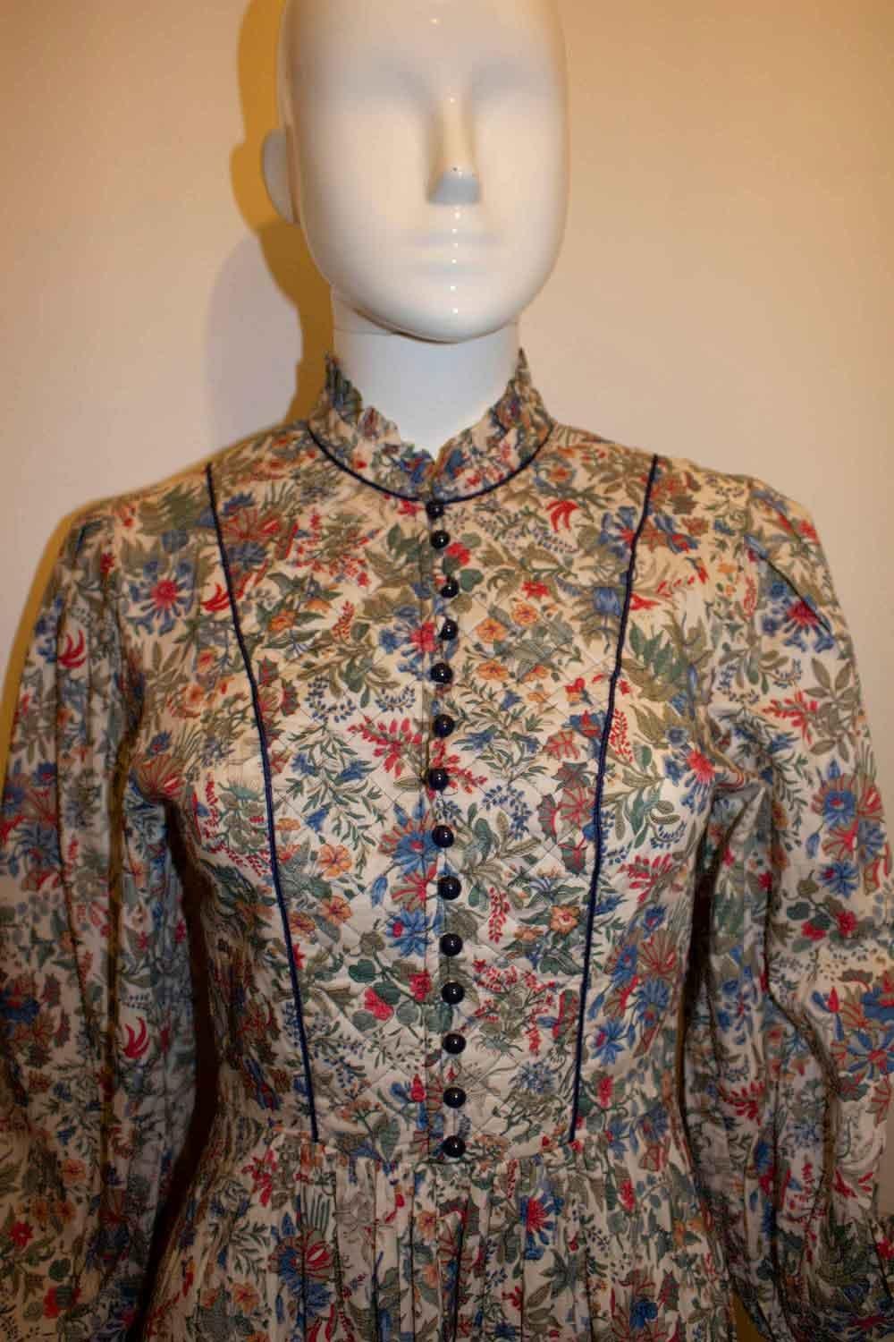 A very pretty vintage dress by Liberty . In lawn cotton the dress has ruffle detail at the neck, quilt detail on the front and cuffs, a front button opening and a back zip plus a self fabric tie belt. 
It is unlined. Size 10 measurements : bust up