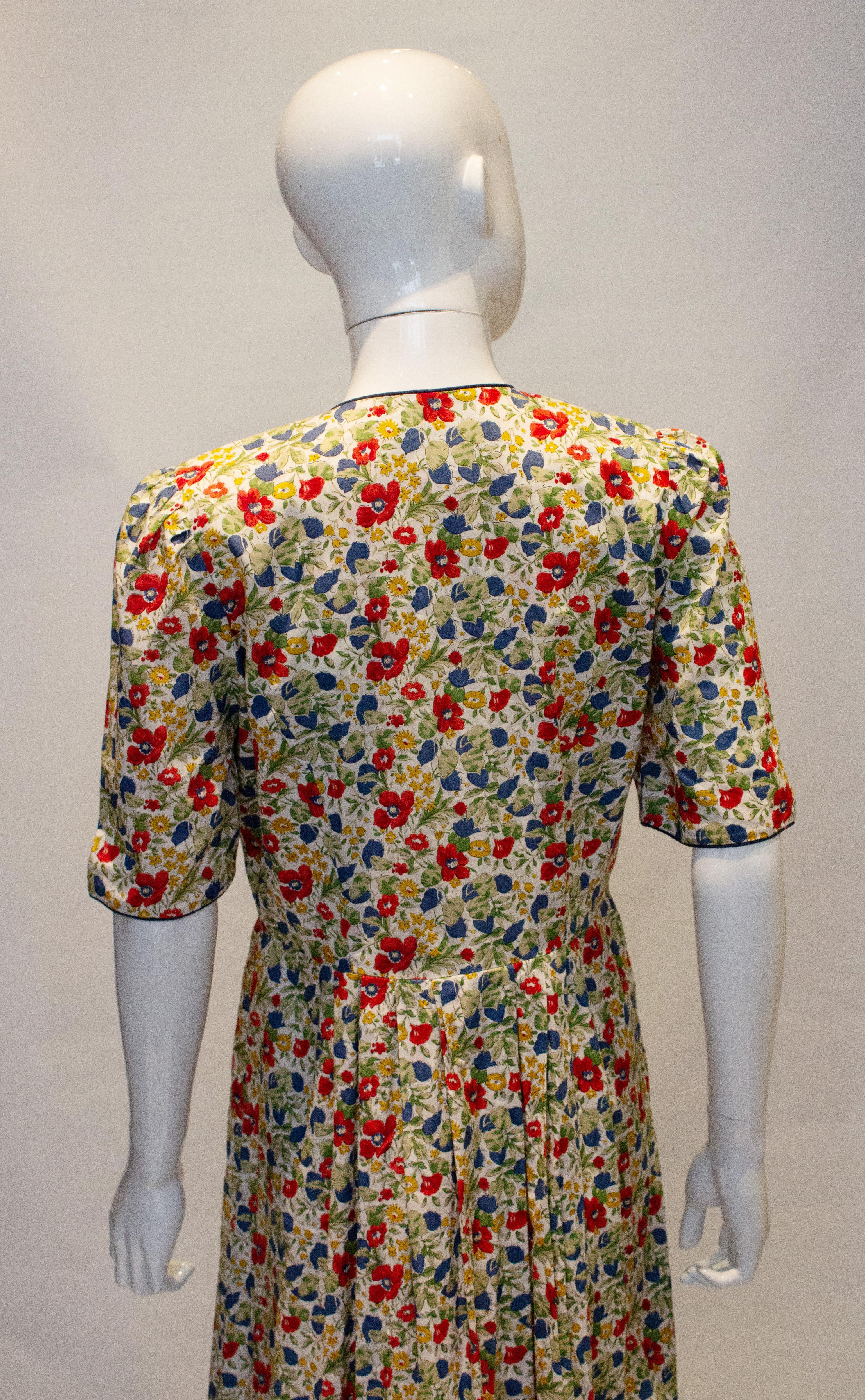 Hübsches Vintage-Kleid aus Baumwolle von Liberty.  Das Kleid ist mit einem Blumenmuster bedruckt und hat einen blauen Saum. Es wird mit einem Knopf geöffnet:: hat zwei Taschen und Falten in der Taille. 
Abmessungen: Büste bis zu 40'':: Taille 31''::