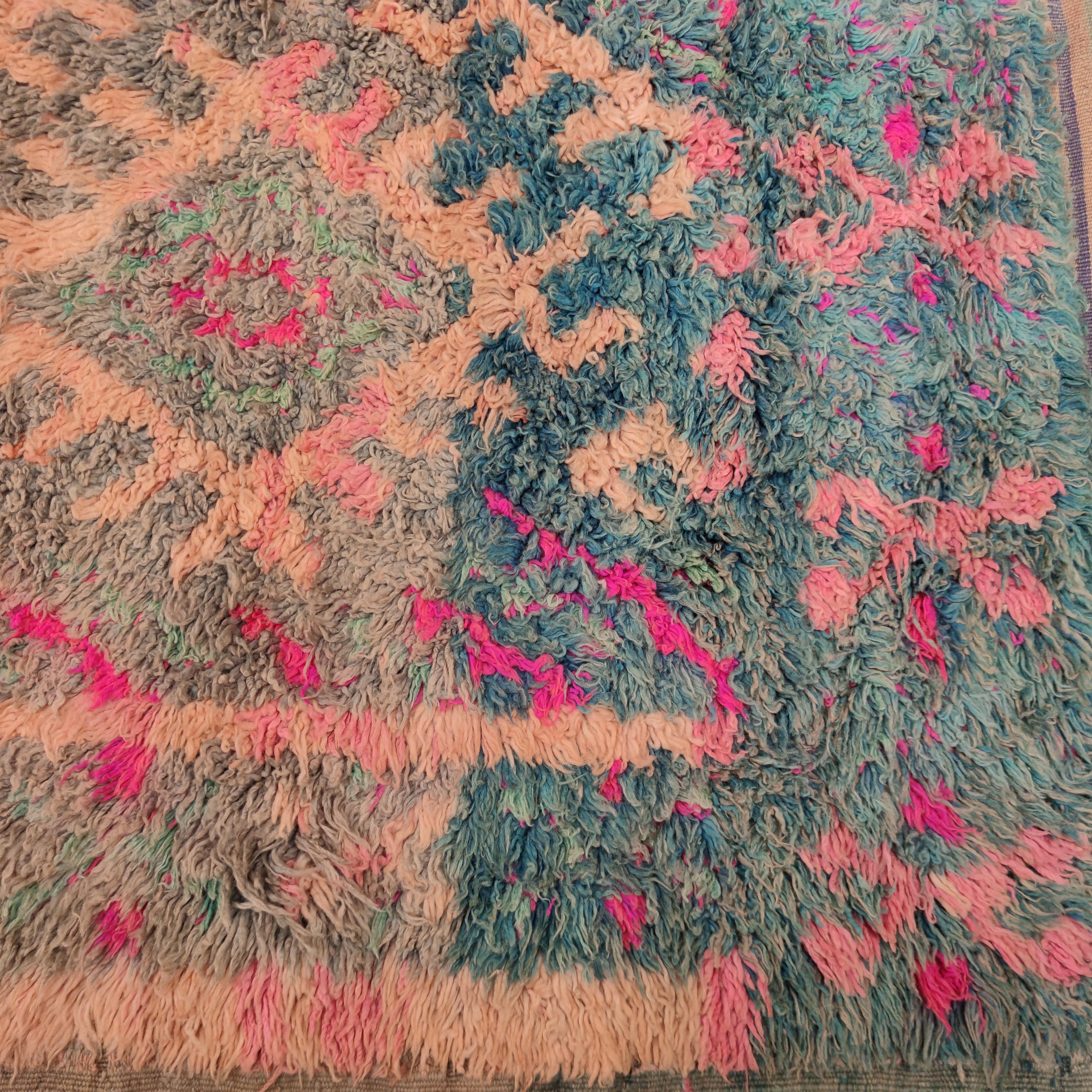 Distinguished by a very unusual palette composed of a blue-grey background and a design in various shades of pink, this Moroccan Berber rug originates from the area of Talsint, located in eastern Morocco near the border with Algeria, which is a